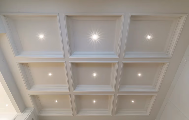 This Richmond Hill interior renovation highlights a refined living space with a coffered ceiling, custom wainscoting, and detailed hardwood flooring with inlay borders. Large windows with plantation shutters enhance natural light, while classic millwork and clean architectural lines create a timeless, elegant interior renovation result.