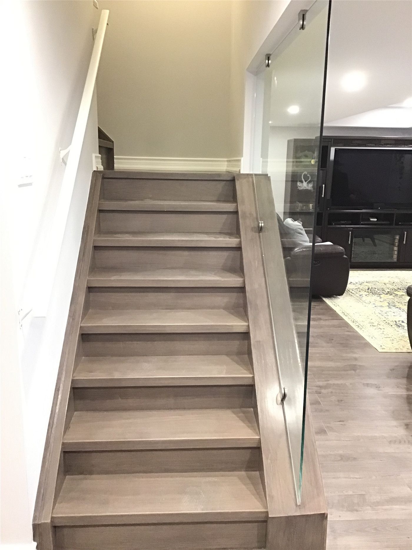 Aurora basement renovation featuring custom wood staircase steps paired with sleek glass railing panels for a contemporary open look. The coordinated flooring finish creates seamless visual flow between levels, enhancing both safety and design appeal. Installed by a professional Toronto renovation company with precision craftsmanship and attention to structural detail.