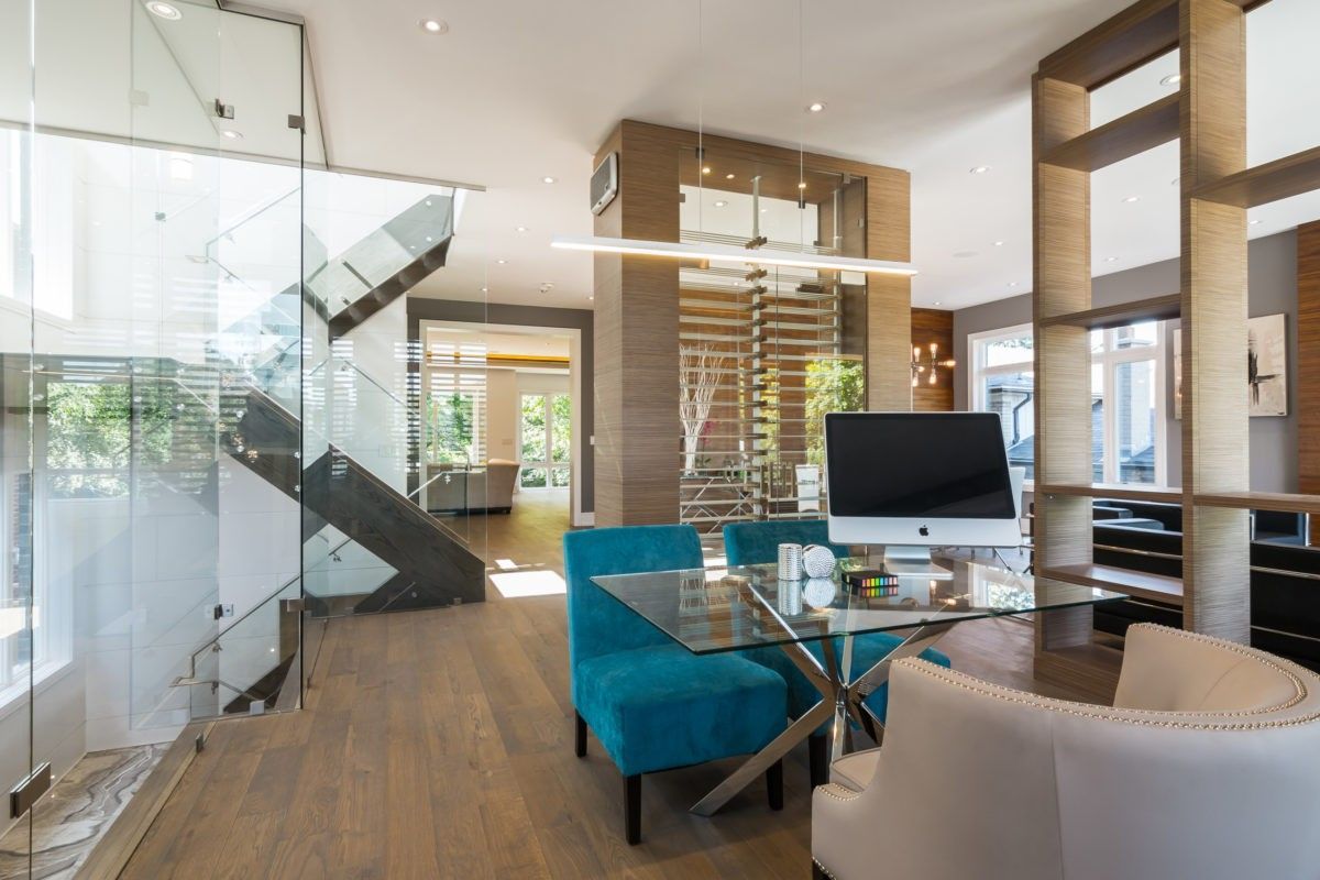 This Toronto modern interior renovation features a stylish home office area integrated within an open-concept layout. The space includes a sleek glass desk, contemporary seating, and a striking glass staircase with metal accents. Natural light and clean architectural lines create a functional yet elegant workspace within a luxury residential setting.