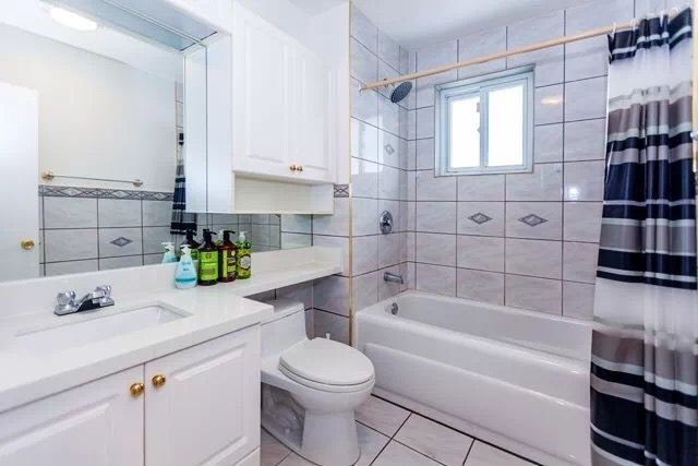 This bathroom interior renovation project in Toronto showcases a clean and functional layout featuring a white vanity cabinet, integrated mirror, and a standard bathtub with tiled surround. The neutral color palette enhances brightness, while the practical design ensures comfort for everyday use. This renovation reflects the quality craftsmanship of a professional Toronto Renovation Company, combining durability, simplicity, and modern living needs.