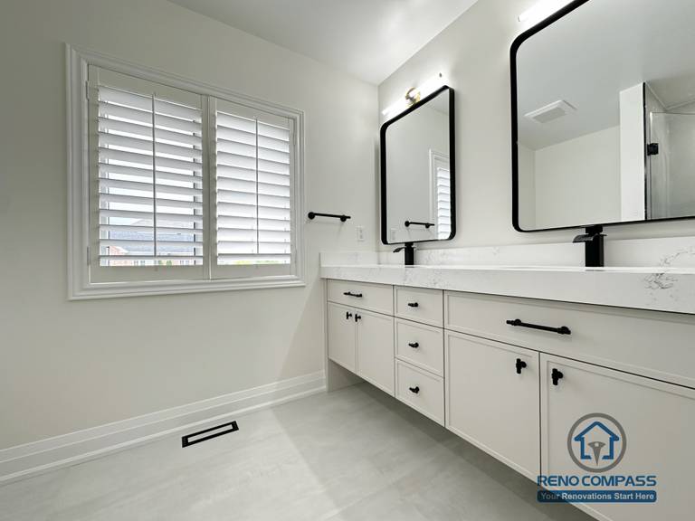This Markham bathroom renovation features a spacious double vanity with quartz countertops, matte black fixtures, and oversized mirrors. Natural light from the large window enhances the clean layout, creating a bright and comfortable bathroom designed for daily use and long-term durability.