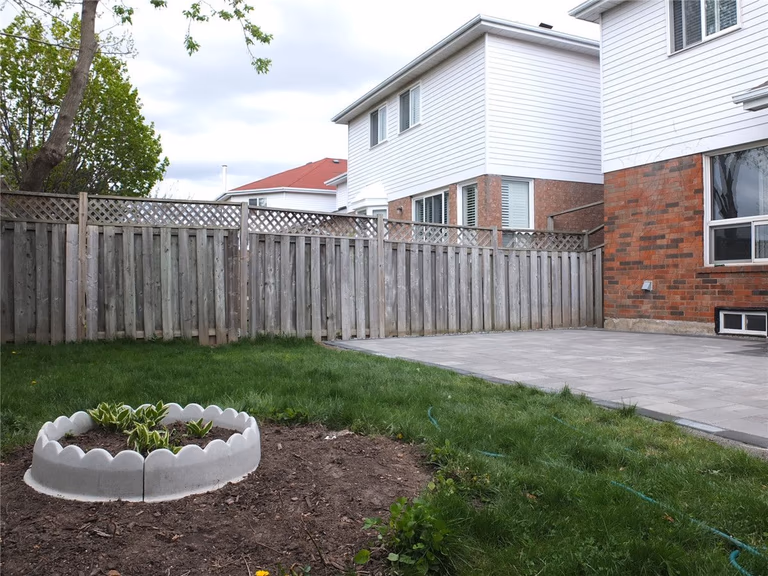 A completed backyard landscaping project in Mississauga featuring a newly installed interlocking stone patio, green lawn area, and decorative garden bed. The grey patio pavers create a clean and durable outdoor space while the surrounding landscaping adds natural balance to the backyard design. Completed by a professional Toronto Renovation Company, Reno Compass Inc., specializing in interlocking patios, landscaping, and exterior home upgrades across the GTA.
