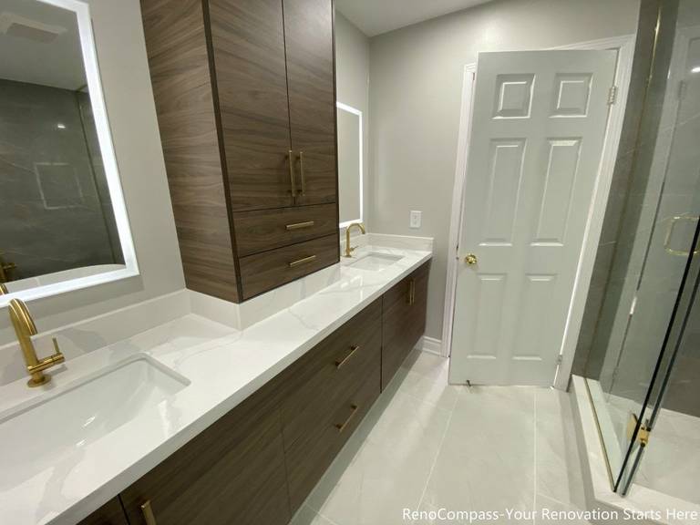 This Oakville master bathroom renovation features a modern double-sink vanity with custom wood cabinetry, quartz countertop, and elegant brushed gold fixtures. The spacious layout includes integrated storage towers, LED mirrors, and a clean tile floor design that enhances both functionality and visual appeal. Designed and completed by a professional Toronto renovation company, this bathroom upgrade delivers a balance of luxury, storage efficiency, and contemporary style, creating a bright and comfortable space that adds long-term value to the home.