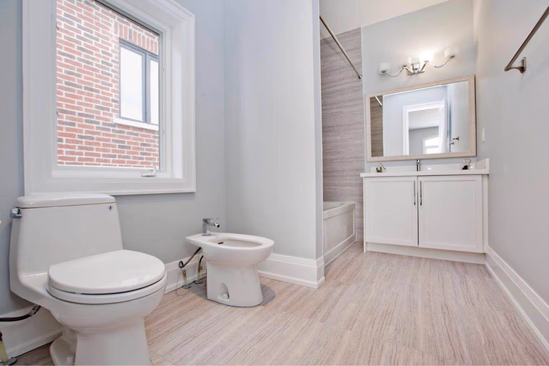 Modern bathroom completed as part of a Toronto design build and whole house renovation Toronto project, featuring a clean vanity design, bathtub with tiled wall finish, large window for natural light, and durable flooring. This renovation reflects the attention to detail and craftsmanship delivered by a professional Toronto Renovation Company, creating a bright, functional, and comfortable bathroom space for everyday living.
