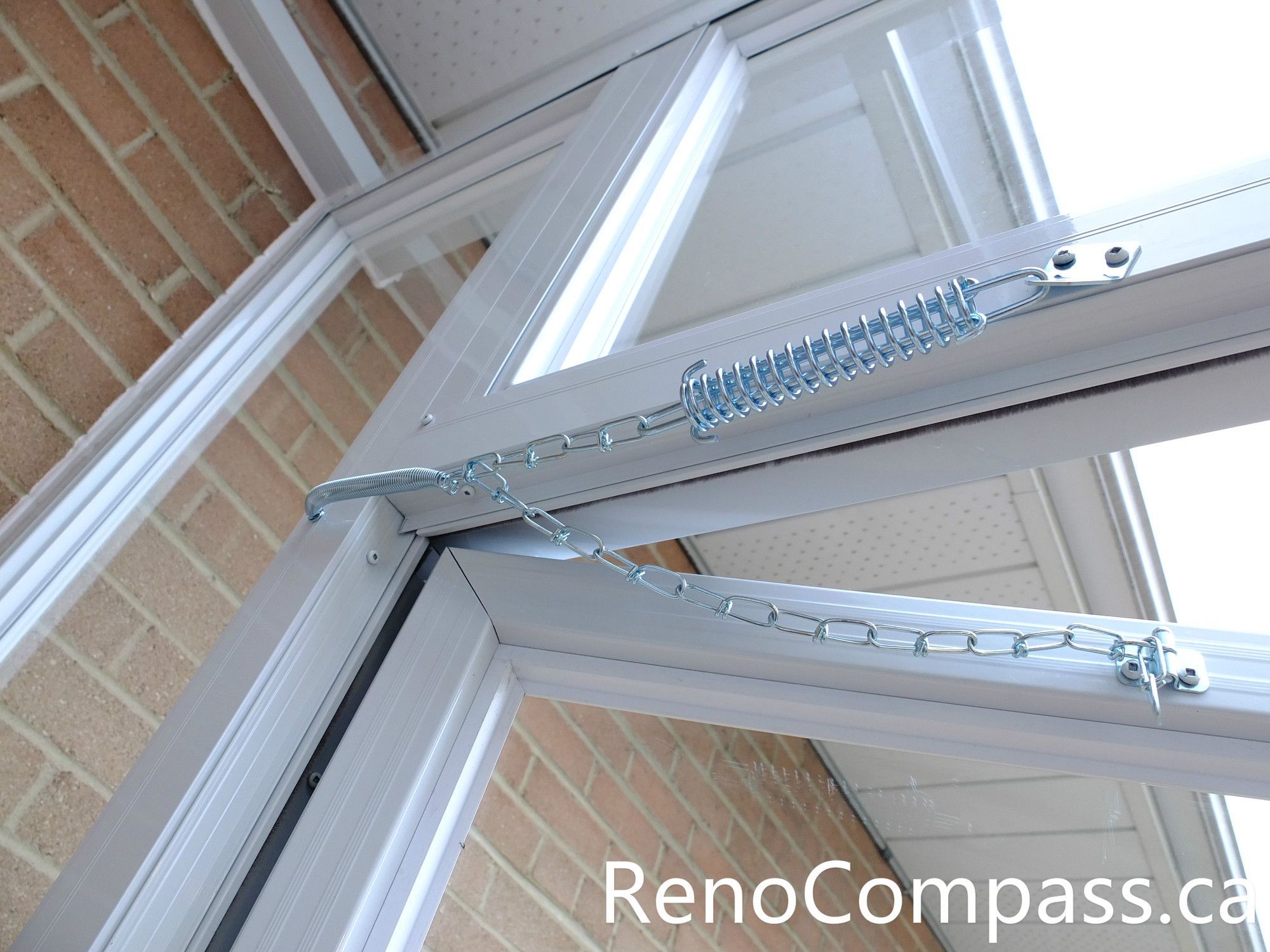 Close-up detail of a storm door closer, safety chain, and aluminum frame connection in a North York storm door installation project. This image highlights the secure hardware setup designed to control door movement, prevent overextension, and improve long-term durability. The professionally installed glass entry enclosure integrates seamlessly with the brick exterior, ensuring smooth operation, structural stability, and enhanced weather protection for the front entrance.