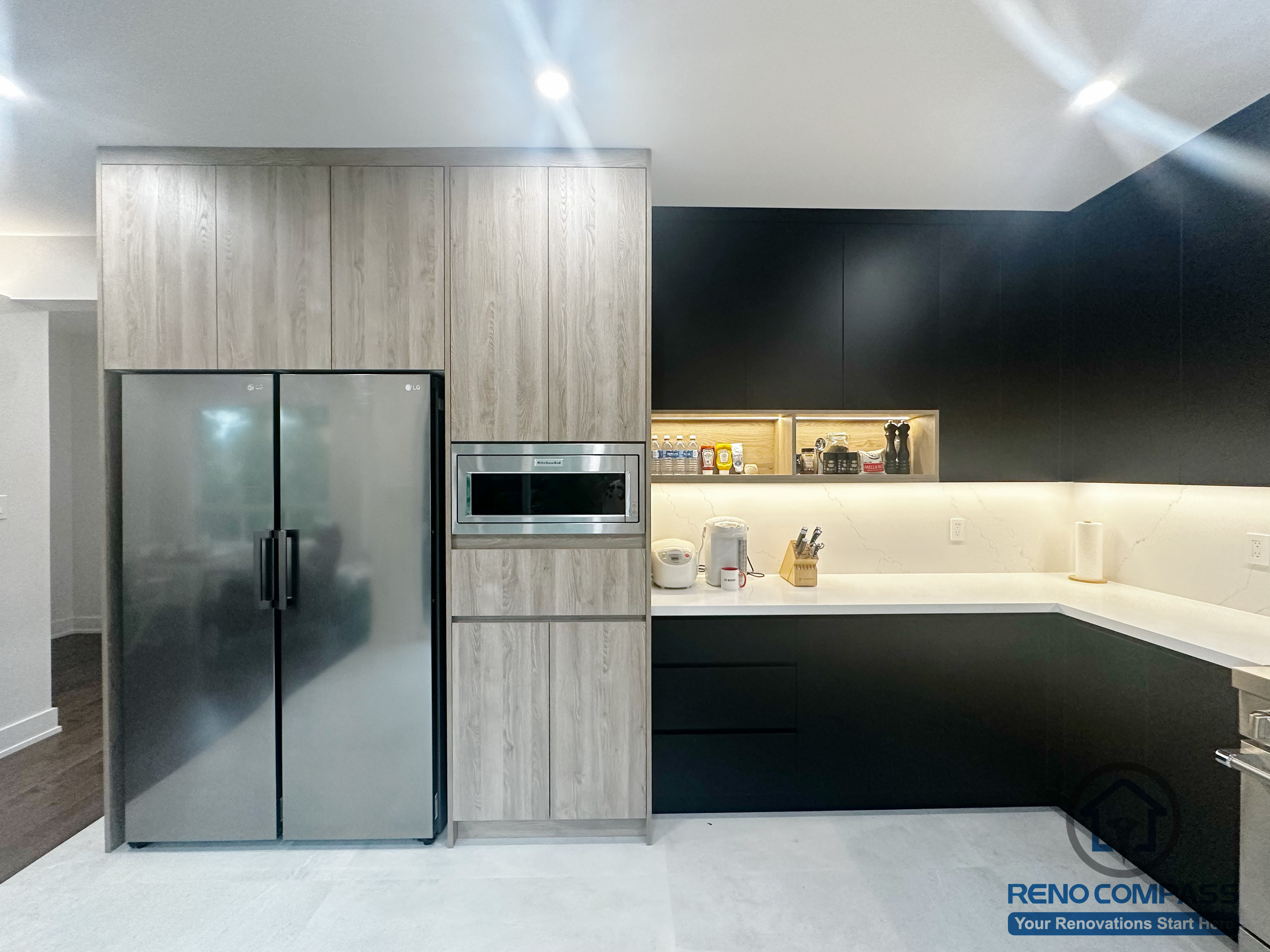 This Oakville interior renovation presents a modern kitchen designed with integrated wood-grain cabinetry and matte black lower storage for a clean, structured appearance. Built-in appliances are seamlessly incorporated into the cabinet wall, maximizing storage efficiency while maintaining a streamlined look. Under-cabinet lighting enhances both functionality and depth along the countertop workspace. The combination of contrasting finishes and minimal detailing emphasizes clarity, balance, and long-term usability, making this kitchen well suited for everyday cooking and modern family living.