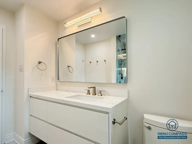 A clean and modern bathroom vanity featuring a wide mirror, integrated LED lighting, and a sleek double-sink quartz countertop. Soft white tones and brushed-gold fixtures create a bright, contemporary look. Part of a full bathroom renovation completed in North York by Reno Compass.
简洁现代的浴室洗手台设计，搭配大尺寸镜子、LED 灯光与石英台面。整体以柔和白色和金色龙头为主，空间明亮高级。此为 Reno Compass 在北约克完成的全套浴室翻新项目之一。
