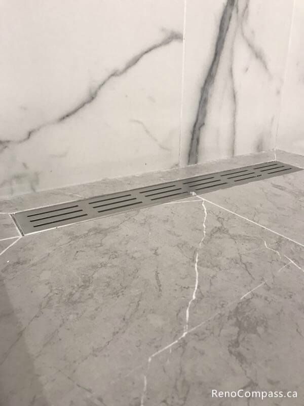This Markham bathroom renovation detail showcases a modern linear shower drain installed with large-format marble-look floor tiles. The sleek drain design improves water drainage efficiency while maintaining a clean, minimalist shower floor appearance, perfectly complementing the contemporary tile layout and overall bathroom upgrade.