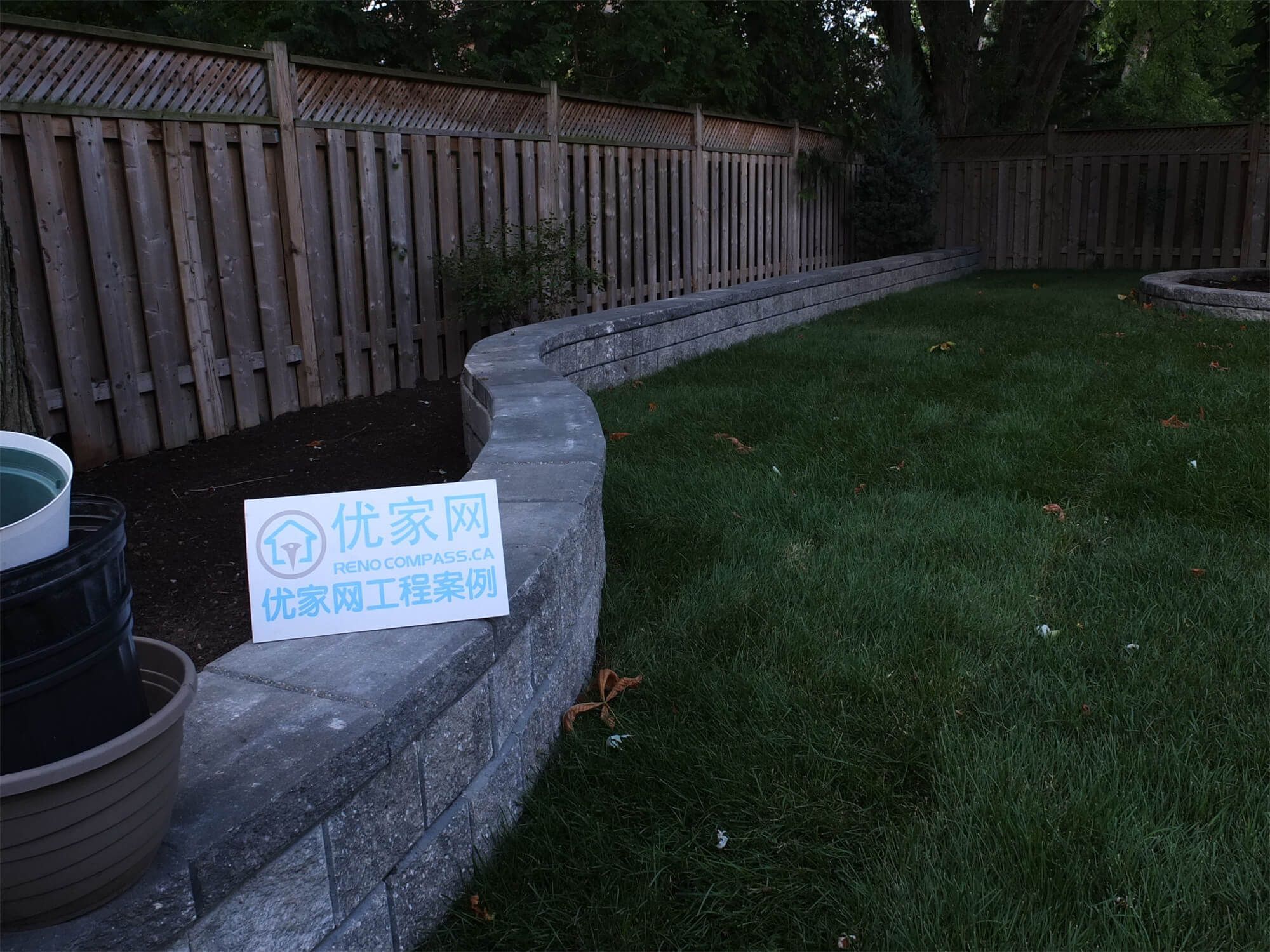 This North York backyard landscaping project features a custom curved retaining wall constructed with durable stone blocks, creating a clean separation between lawn and planting areas. The smooth curve design enhances the visual flow of the backyard while providing structural support and improved drainage. Paired with a wooden privacy fence and neatly maintained grass, the space offers both function and aesthetic appeal. Completed by Reno Compass, this project highlights professional craftsmanship in retaining wall construction, backyard landscaping, and residential outdoor renovation in North York.