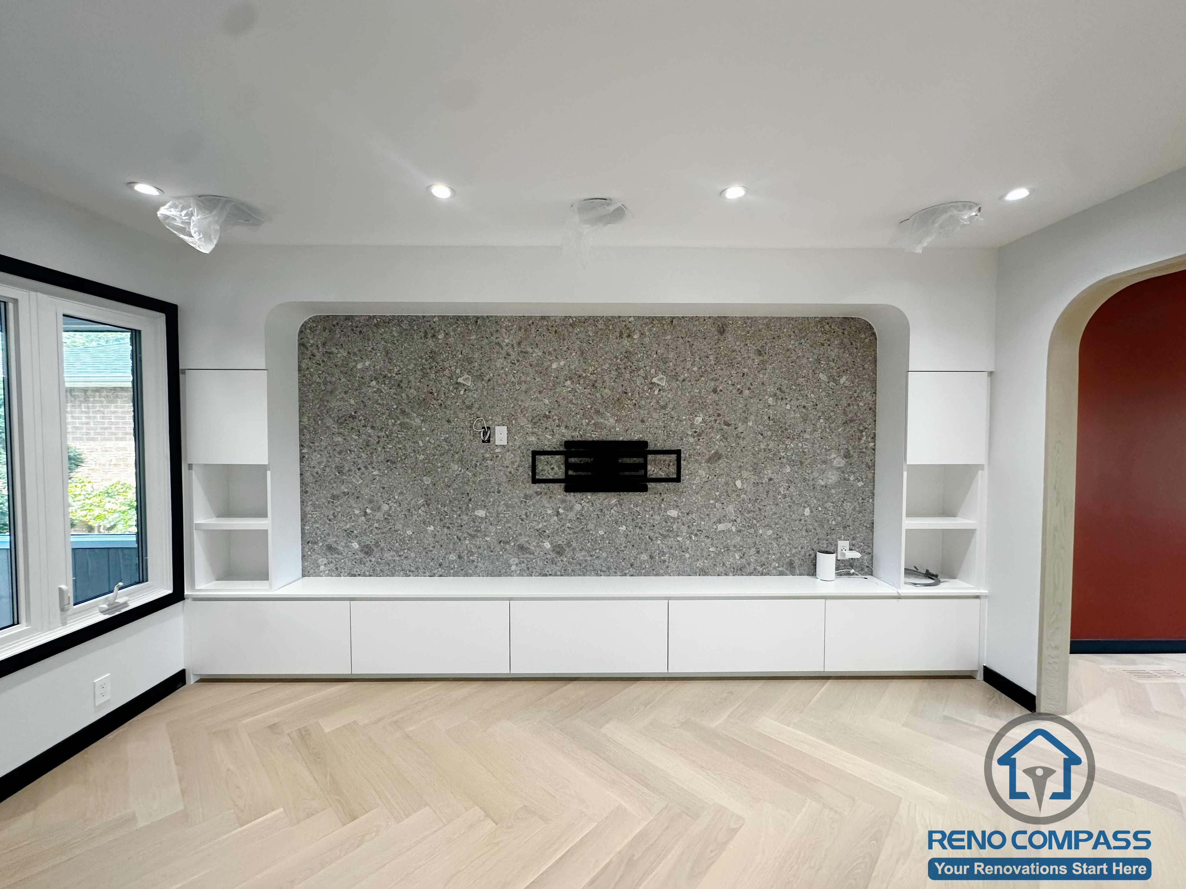 This image highlights the modern feature TV wall from our Richmond Hill living room renovation.
The textured stone panel creates a strong focal point, paired with symmetrical open shelving and custom white cabinetry for a clean, contemporary look.
The extended lower drawers offer generous storage, making this a great reference for