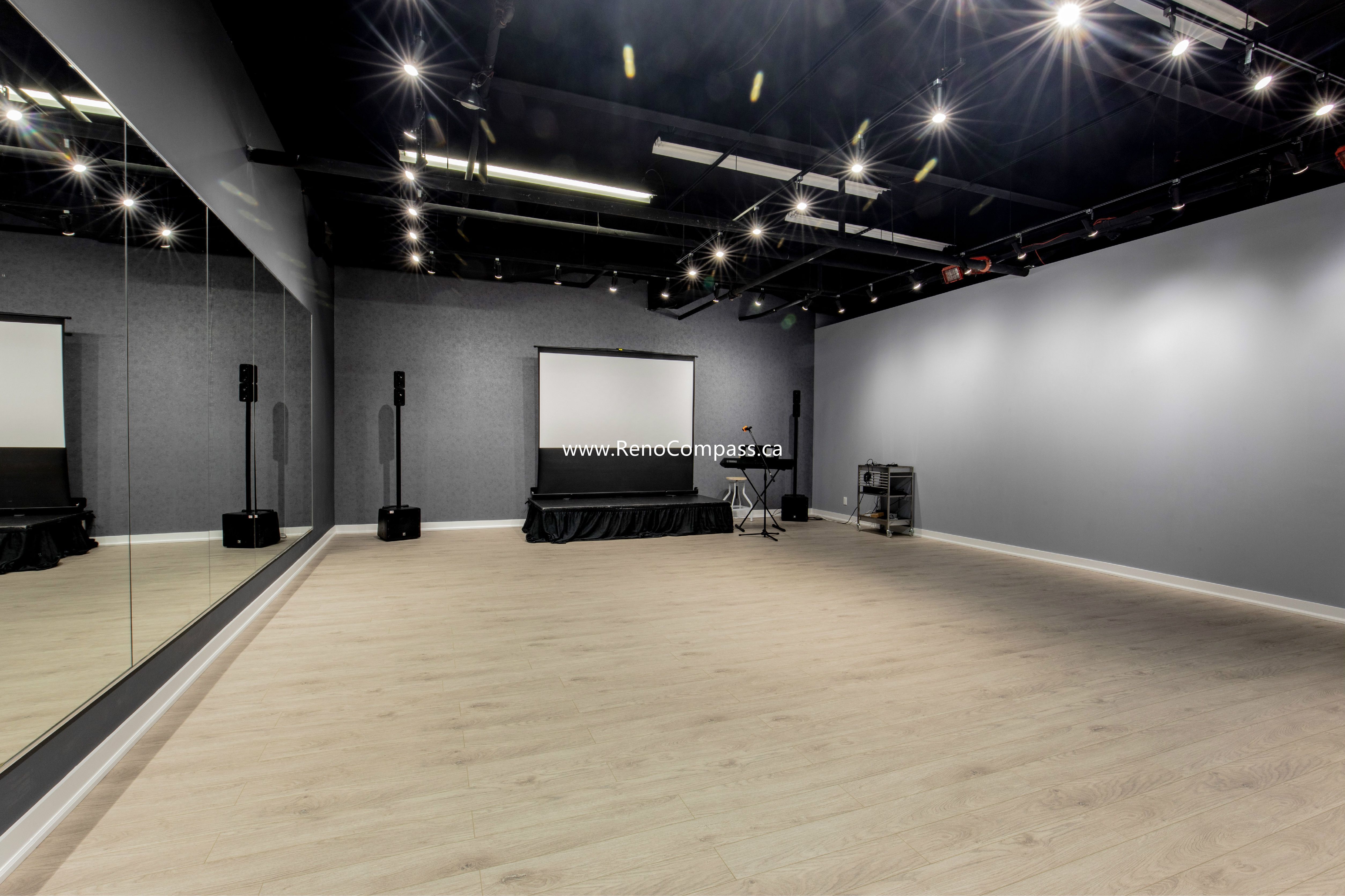 A spacious commercial studio renovation featuring luxury vinyl plank flooring, full-length mirrors, and professional track lighting. This Richmond Hill project showcases a modern industrial aesthetic with an exposed black ceiling, perfect for music schools and dance studios.