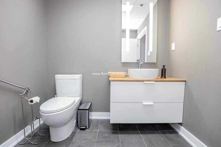 A professional commercial bathroom renovation featuring a modern floating vanity with a vessel sink, grey porcelain tile flooring, and ADA-compliant grab bars. Designed for comfort and style at The Singing School in Richmond Hill.