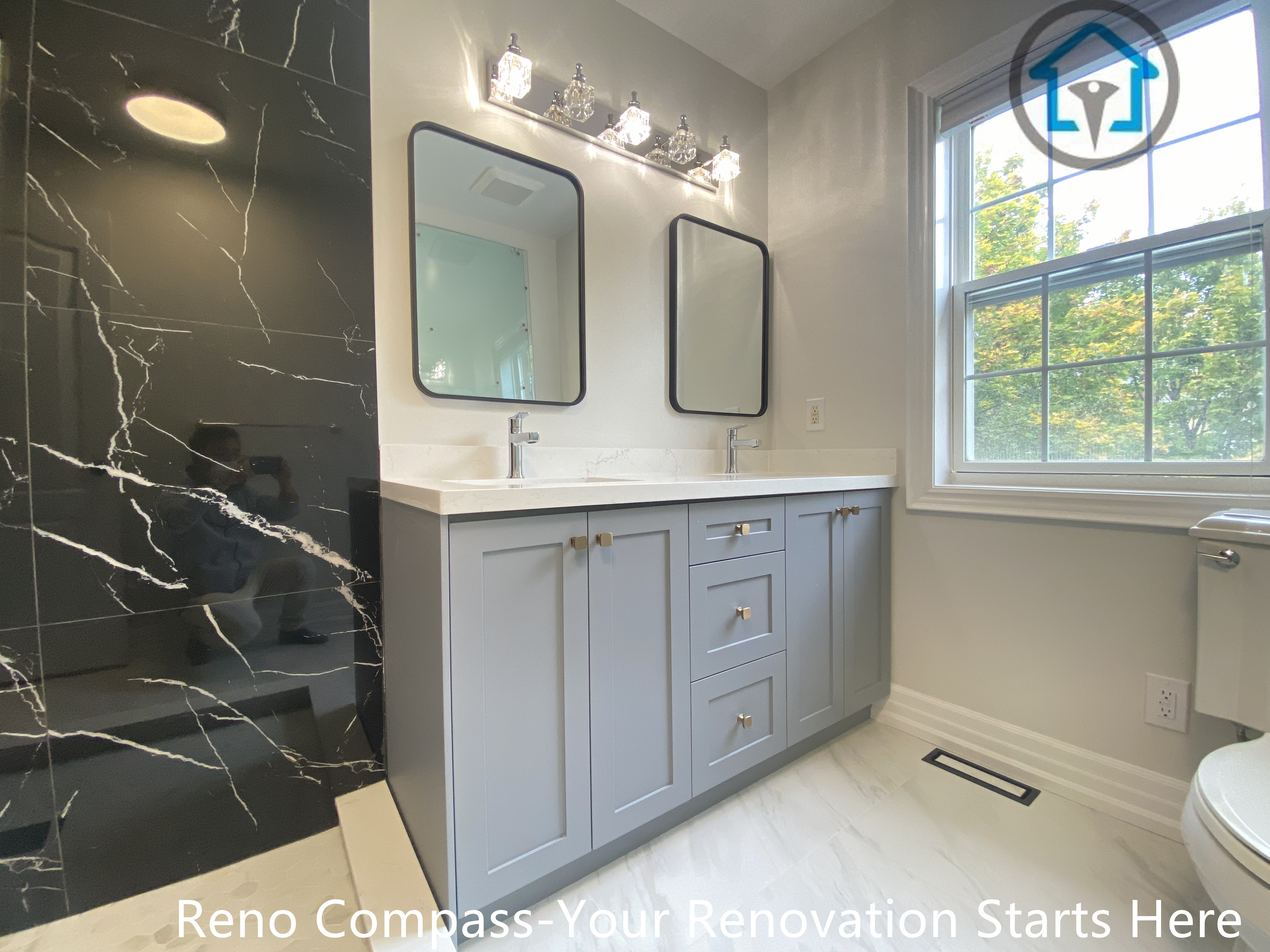 This double vanity design combines soft grey cabinetry with a striking black marble–look accent wall to create contrast and visual depth. Rectangular mirrors and balanced lighting enhance symmetry, while the large window introduces natural light that keeps the space bright and inviting. The layout is both functional and refined, designed for comfortable daily use.
