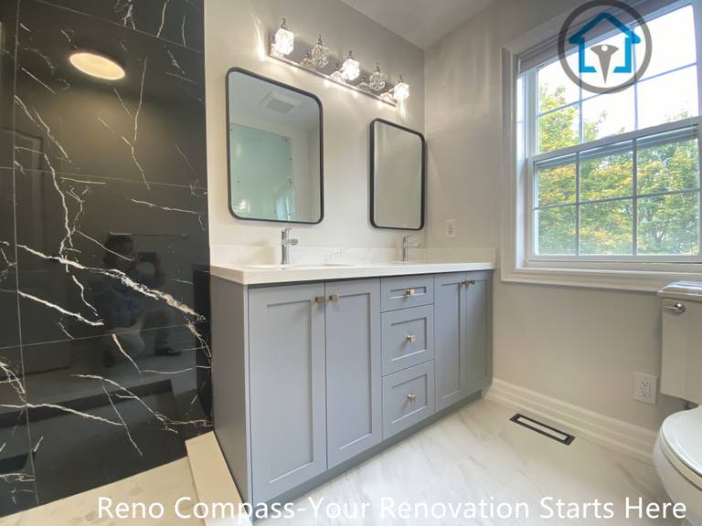 This double vanity design combines soft grey cabinetry with a striking black marble–look accent wall to create contrast and visual depth. Rectangular mirrors and balanced lighting enhance symmetry, while the large window introduces natural light that keeps the space bright and inviting. The layout is both functional and refined, designed for comfortable daily use.