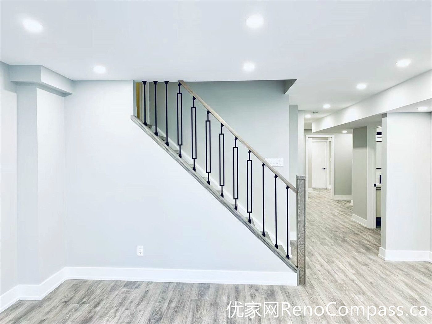 This Markham renovation showcases a clean basement interior featuring a modern staircase with black metal railings and durable wood-look flooring. The open layout improves flow between spaces, while the neutral tones create a bright and versatile environment suitable for multiple uses.