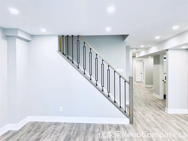 This Markham renovation showcases a clean basement interior featuring a modern staircase with black metal railings and durable wood-look flooring. The open layout improves flow between spaces, while the neutral tones create a bright and versatile environment suitable for multiple uses.