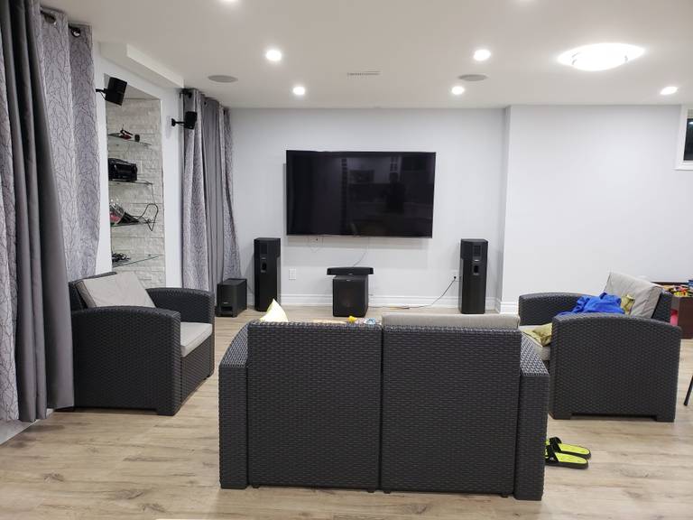 This finished basement renovation in Newmarket, Toronto showcases a modern entertainment and media area designed for comfort and functionality. The space features upgraded flooring, recessed pot lights, and a wall-mounted large screen TV with a full home theater speaker setup. Custom built-in shelving with glass accents adds storage and display functionality, while neutral wall tones and layered lighting create a clean, contemporary feel. The open-concept layout allows for a comfortable lounge and family gathering space, making the basement ideal for movie nights and daily living. Completed by a professional Toronto renovation company, this project highlights practical design, durability, and modern basement living.