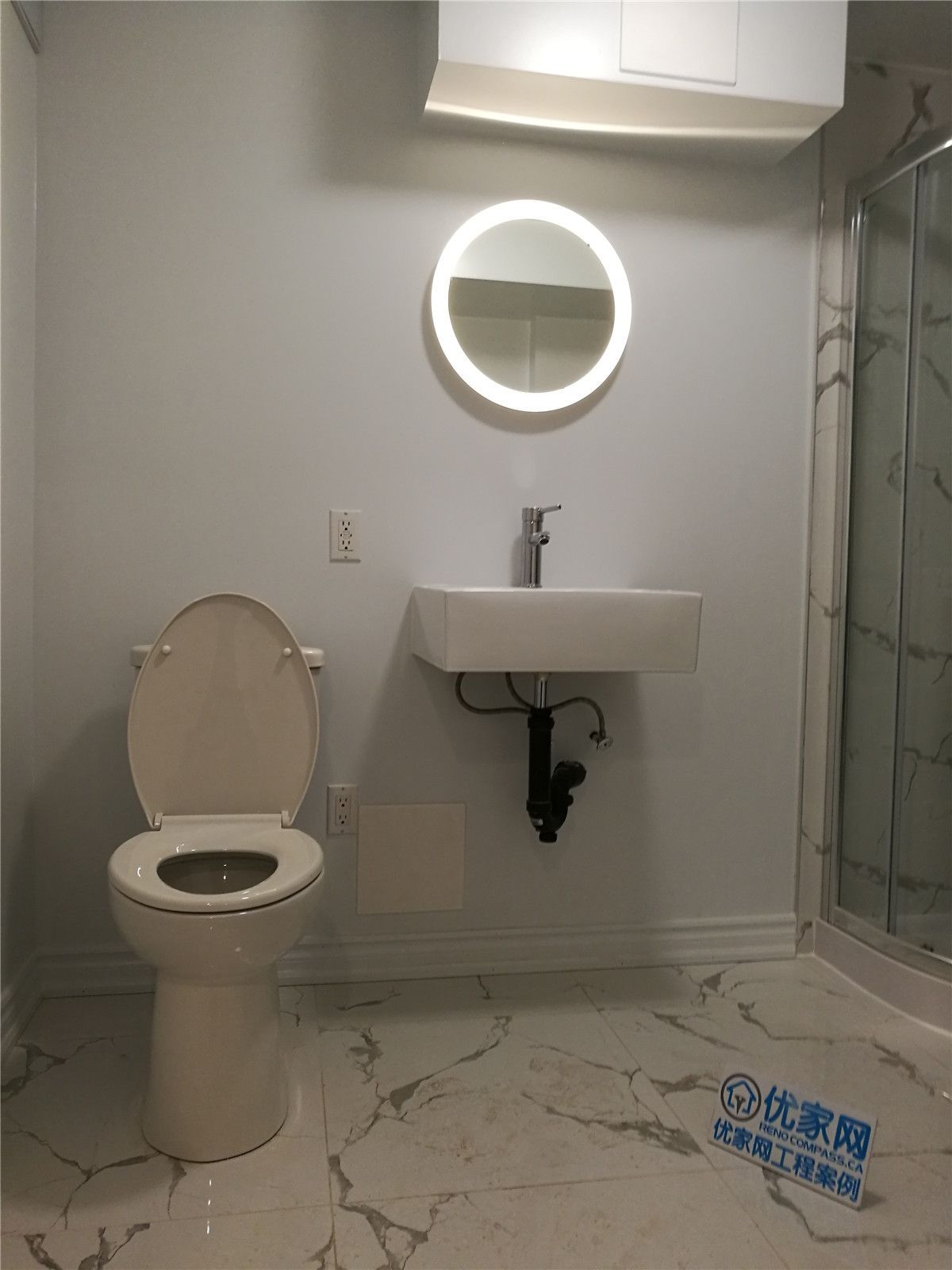 Modern basement bathroom renovation in Markham featuring marble-style floor tiles, sleek wall-mounted vanity, LED round mirror, and glass shower enclosure. This clean and contemporary bathroom design enhances comfort, functionality, and property value, completed by a professional Toronto renovation company serving the GTA.