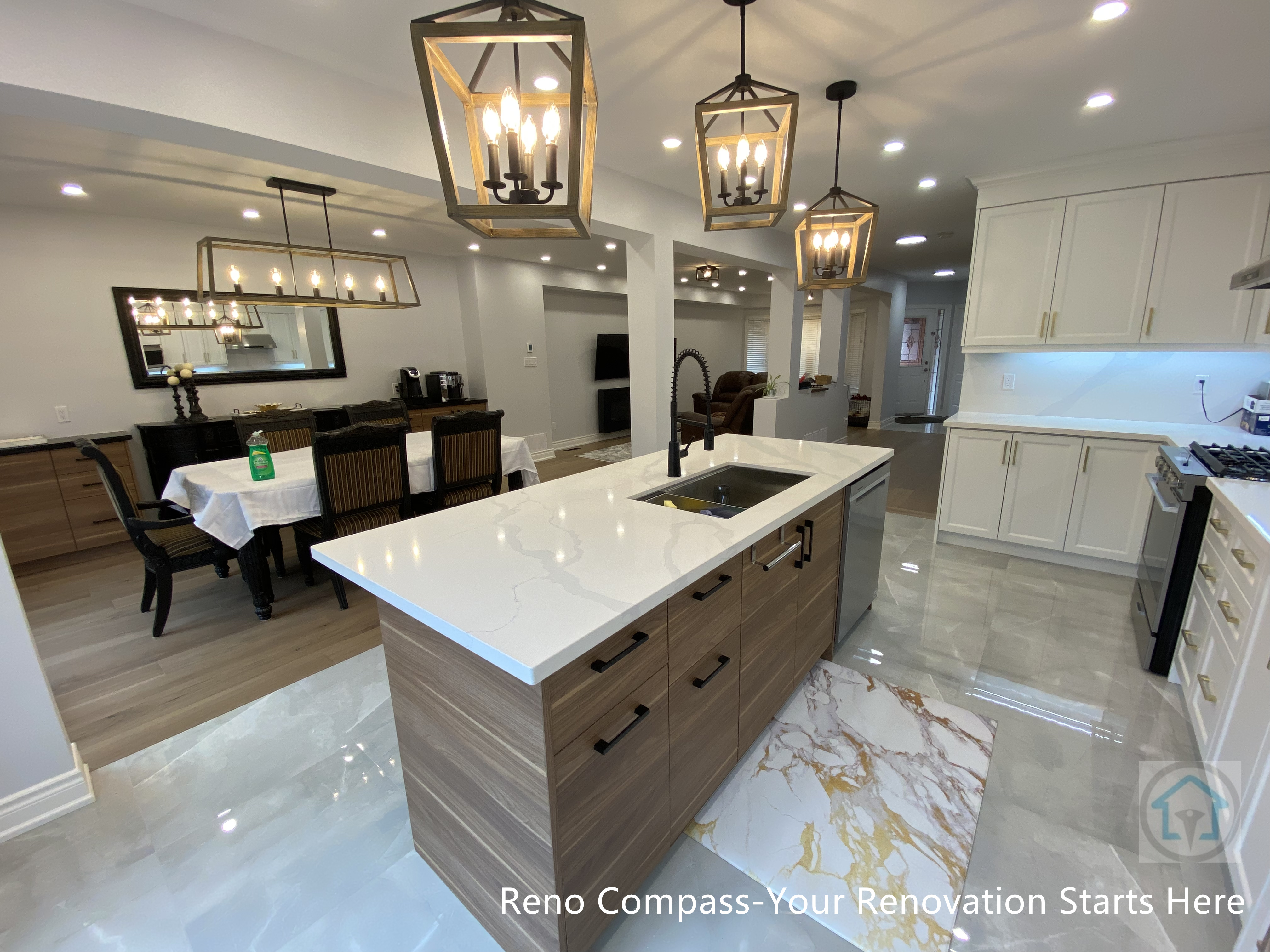 This Newmarket interior renovation showcases a spacious open-concept kitchen centered around a custom-built island with quartz countertop and integrated sink. Warm wood cabinetry contrasts with polished marble-look flooring, creating a balanced and refined aesthetic. Statement lantern-style pendant lights define the kitchen zone while maintaining visual continuity with the adjacent dining area. Recessed ceiling lights enhance brightness and depth throughout the space. Designed and executed by a Toronto renovation company, this project highlights thoughtful layout planning, premium finishes, and seamless integration between kitchen and living areas.