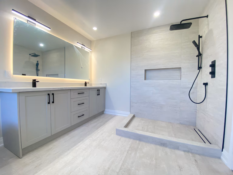 A balanced view of the master bathroom completed as part of a Richmond Hill interior renovation, highlighting the custom vanity and walk-in shower within the same space. This bathroom renovation features integrated vanity storage, LED backlit mirror lighting, a low-profile shower base, large-format wall tiles, and matte black fixtures. Designed and built by Reno Compass, the layout emphasizes clean lines, practical circulation, and cohesive material selection for modern homes in Richmond Hill and the Greater Toronto Area.