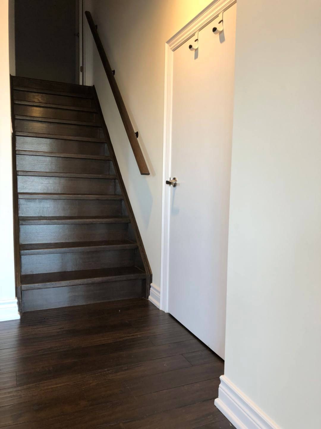 Newly finished hardwood staircase completed as part of a Toronto basement renovation, featuring dark-stained wood treads, matching flooring transition, clean white trim, and modern handrail installation for a seamless connection between levels.