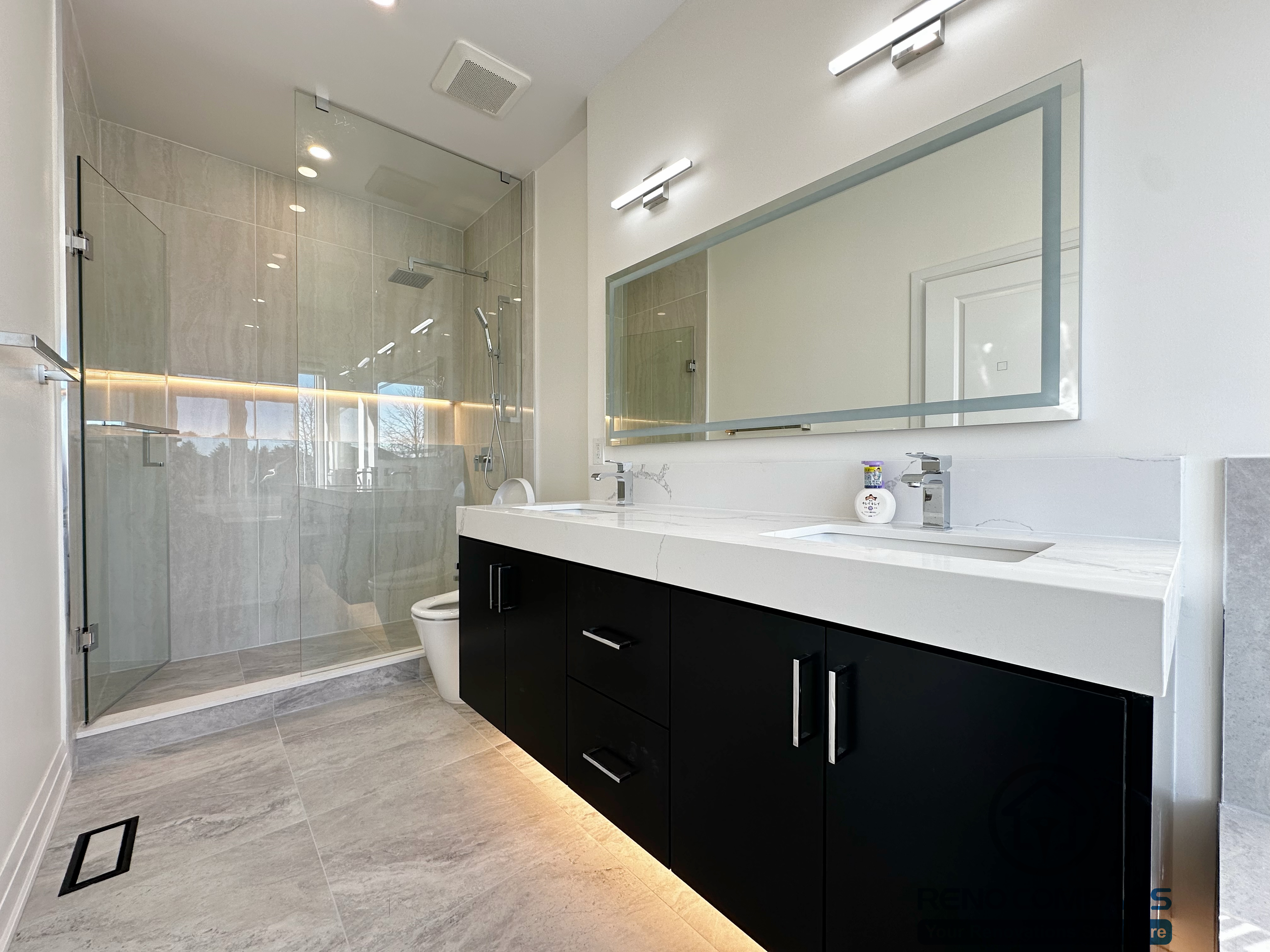 Modern bathroom renovation in Richmond Hill featuring a double-sink vanity with quartz countertop, matte black base cabinetry, integrated under-vanity lighting, and a frameless glass shower enclosure. The layout emphasizes clean lines, durable finishes, and efficient daily use.