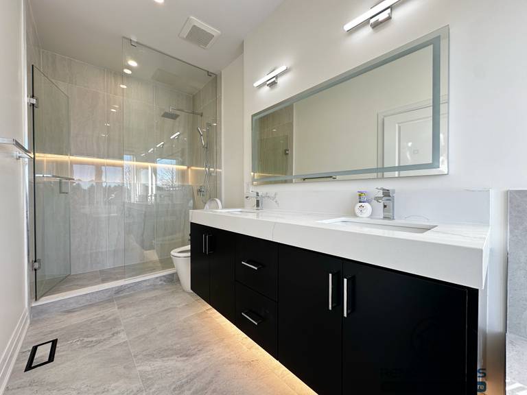 Modern bathroom renovation in Richmond Hill featuring a double-sink vanity with quartz countertop, matte black base cabinetry, integrated under-vanity lighting, and a frameless glass shower enclosure. The layout emphasizes clean lines, durable finishes, and efficient daily use.