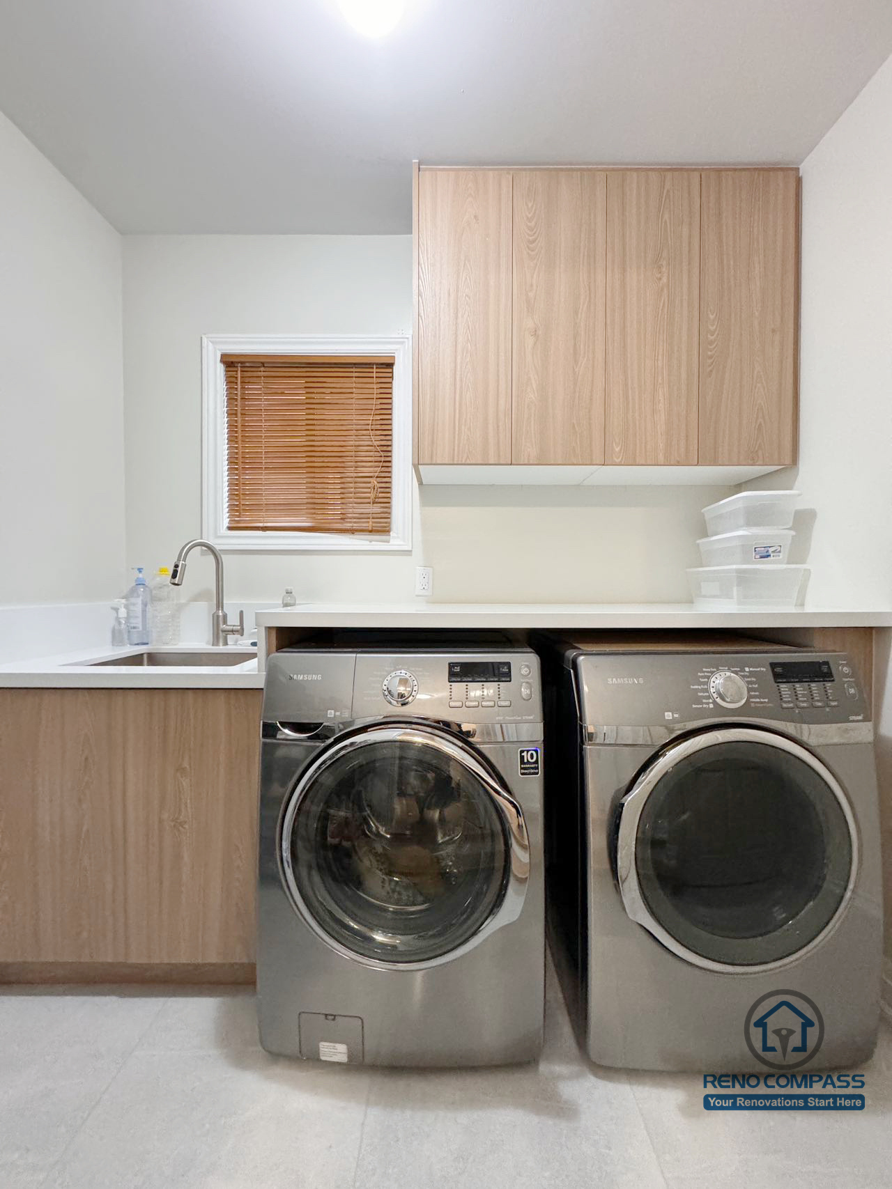 This Mississauga interior renovation showcases a modern laundry room designed for both efficiency and clean aesthetics. Custom wood cabinetry provides ample storage, while the integrated countertop and sink create a practical workspace for daily use. The side-by-side washer and dryer layout maximizes functionality, resulting in a bright, organized, and contemporary laundry area.
