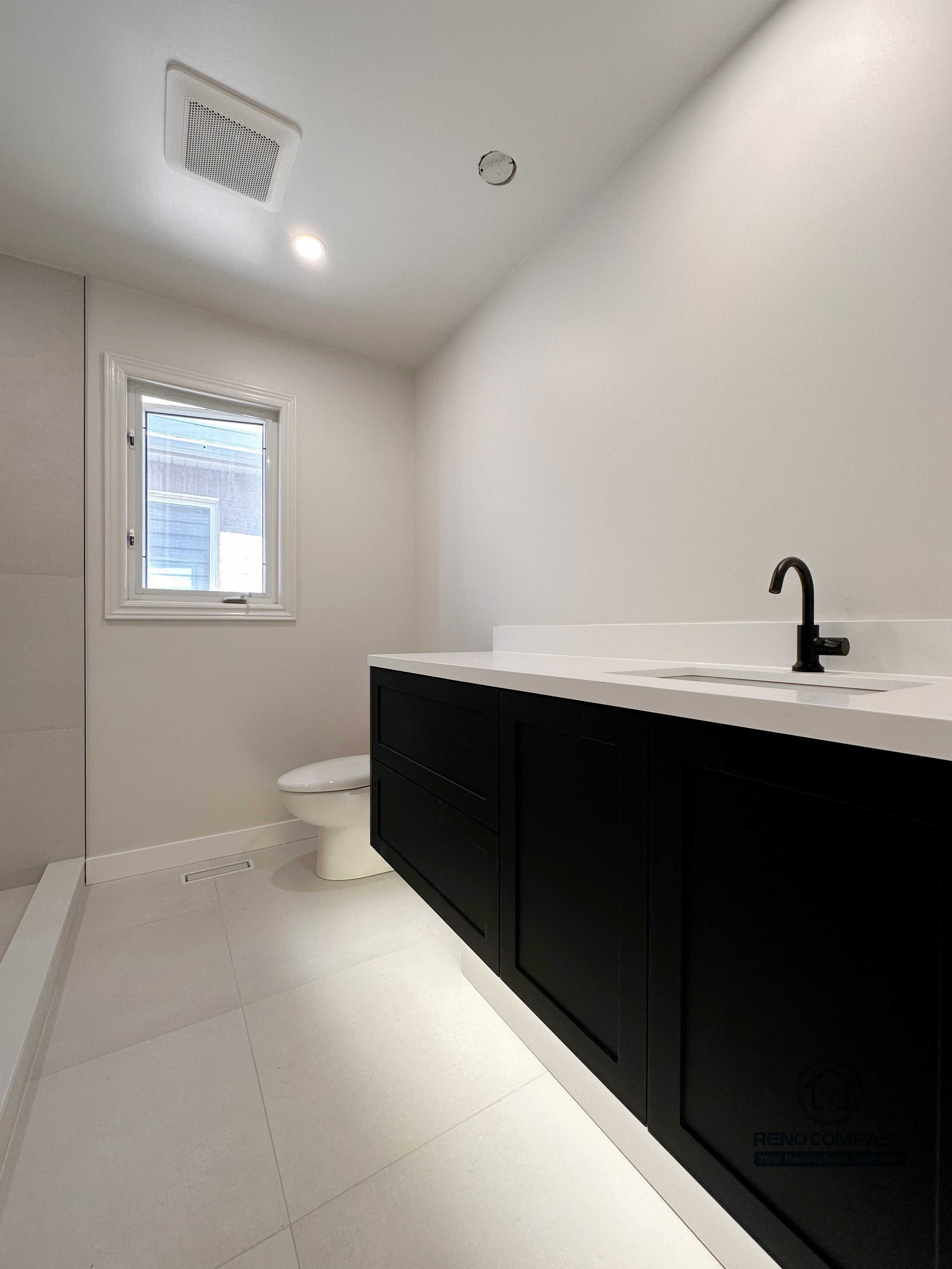Modern bathroom renovation in Markham featuring a sleek black vanity, quartz countertop, and minimalist matte black fixtures. The clean white walls, recessed lighting, and compact layout create a bright, functional powder room designed for everyday use and easy maintenance.