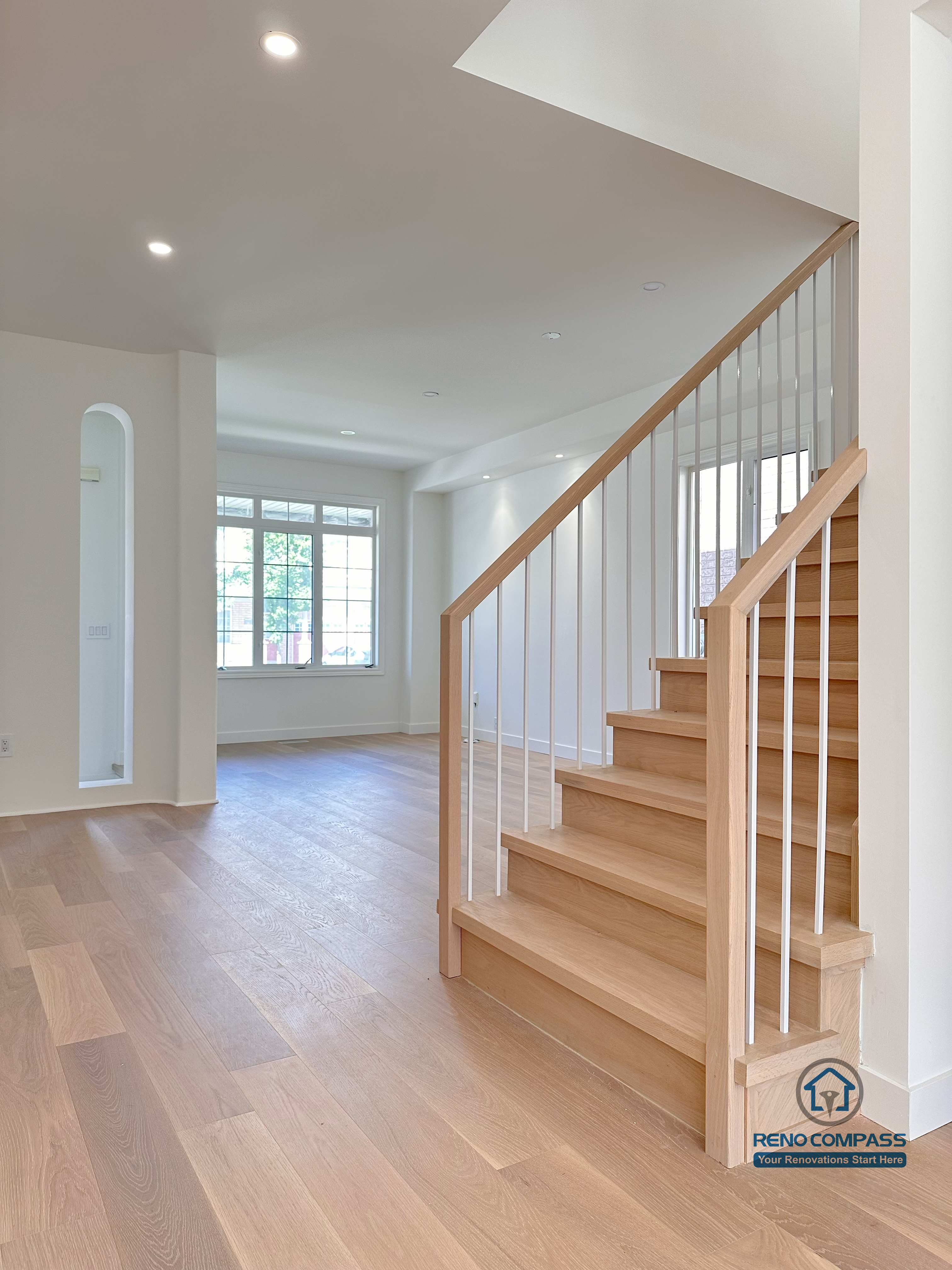 This image showcases a Markham flooring and stair renovation featuring wide-plank hardwood flooring and an open staircase with natural wood treads and white vertical railings. The seamless connection between the staircase and main living area enhances openness, light flow, and spatial continuity. Completed by a professional Toronto renovation company, Reno Compass Inc., the design balances modern simplicity with long-term durability.