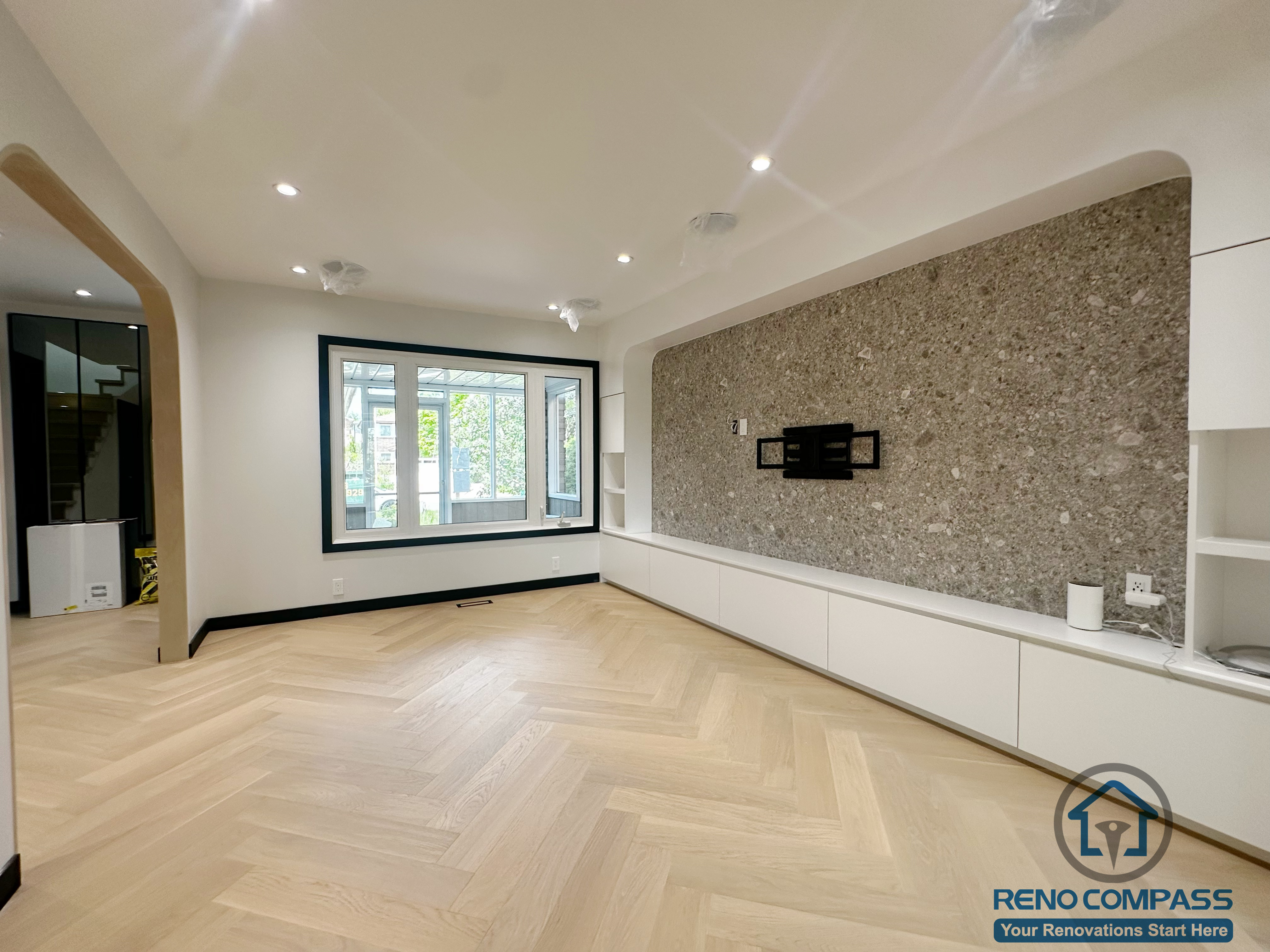 This photo captures the full living room view from our Richmond Hill renovation project.
The light herringbone flooring pairs beautifully with the long modern feature wall, creating a warm, spacious, and contemporary feel.
Large windows bring in natural light, while the stone TV wall and extended white cabinetry offer both style and functionality.