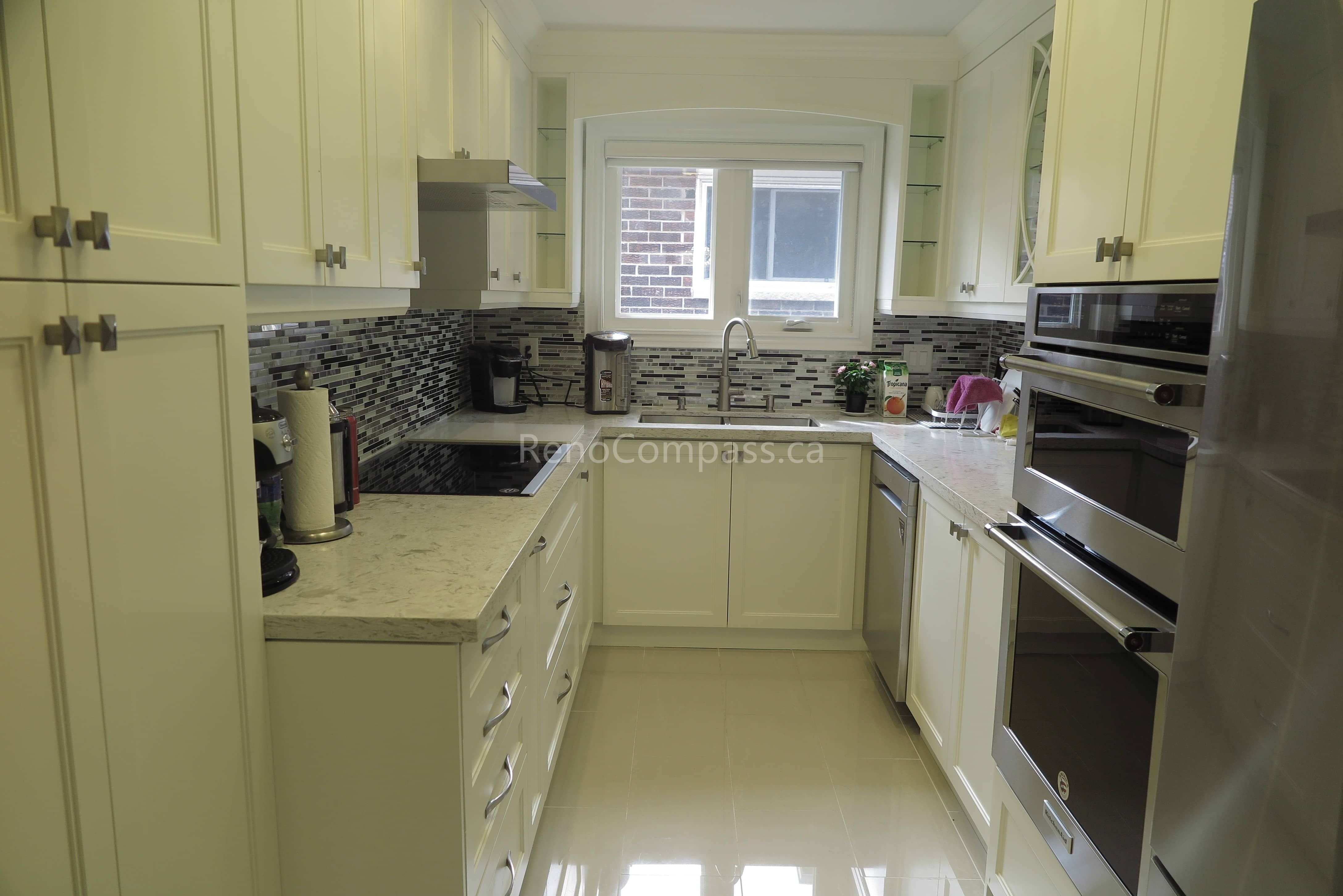 This Toronto interior renovation features a bright modern kitchen with custom white cabinetry, quartz countertops, built-in stainless steel appliances, and a stylish mosaic backsplash. The efficient layout maximizes storage and functionality while maintaining a clean, elegant look. Completed by a trusted Toronto renovation contractor, this project reflects Reno Compass Inc.’s expertise in delivering high-quality kitchen upgrades and refined interior finishes.