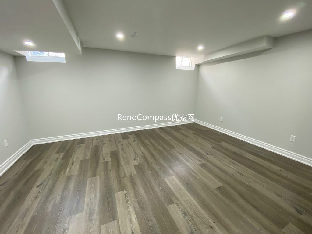 Modern basement renovation in Richmond Hill featuring open layout design, high-quality wooden floors, and elegant white baseboards. Reno Compass transformed this space into a bright and functional lower level.