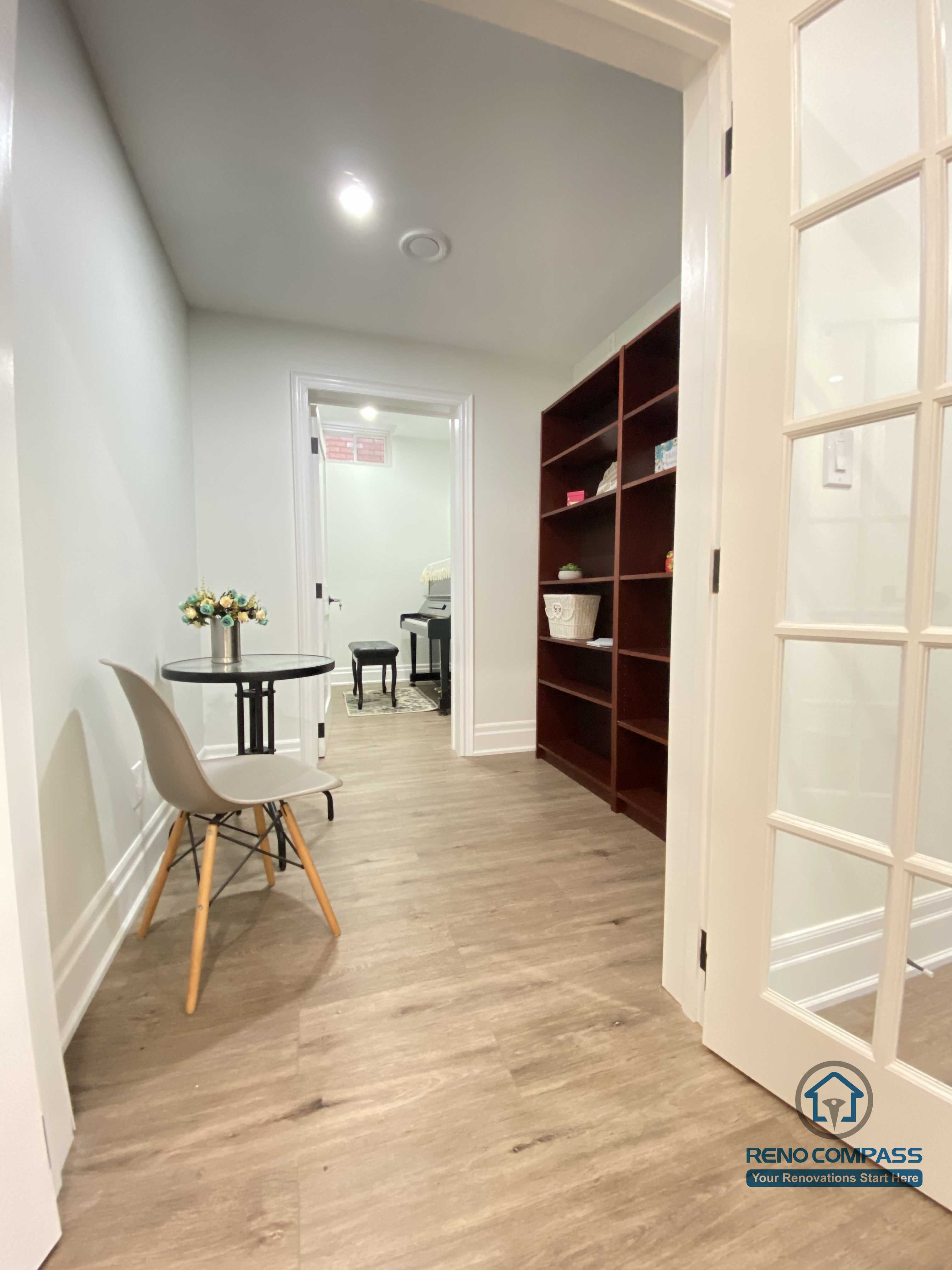 This Oakville basement renovation showcases a clean, functional hallway layout with custom built-in shelving and a compact study nook. Wood flooring runs seamlessly through the space, paired with recessed ceiling lights to maintain a bright and welcoming atmosphere. Glass-panel doors help preserve openness while defining zones for storage, reading, or light work. As an experienced Toronto renovation company, Reno Compass designs basement layouts that balance circulation, storage efficiency, and everyday usability, creating organized and comfortable lower-level living spaces.