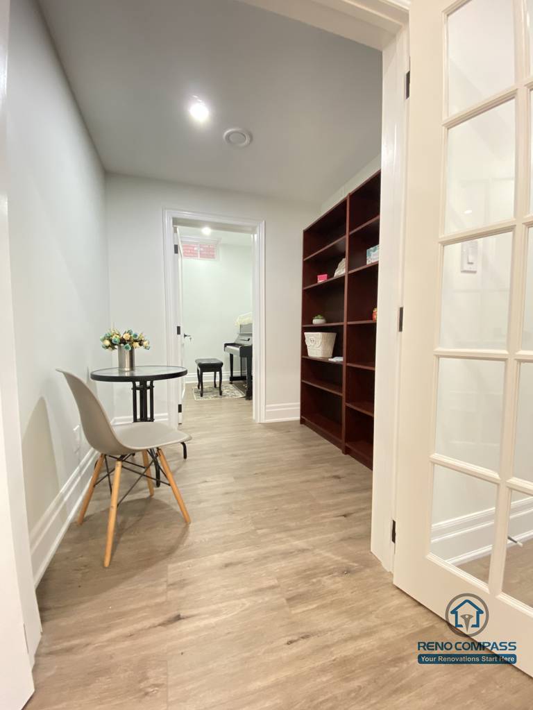This Oakville basement renovation showcases a clean, functional hallway layout with custom built-in shelving and a compact study nook. Wood flooring runs seamlessly through the space, paired with recessed ceiling lights to maintain a bright and welcoming atmosphere. Glass-panel doors help preserve openness while defining zones for storage, reading, or light work. As an experienced Toronto renovation company, Reno Compass designs basement layouts that balance circulation, storage efficiency, and everyday usability, creating organized and comfortable lower-level living spaces.