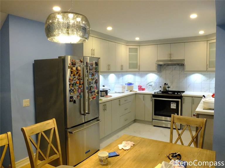 This Aurora kitchen renovation showcases a bright and functional kitchen layout featuring custom white cabinetry, stainless steel appliances, and a marble-pattern backsplash. Recessed ceiling lights and under-cabinet lighting enhance the overall brightness, while the open connection to the dining area creates a comfortable space for family gatherings. The updated kitchen combines modern finishes with practical storage solutions, reflecting the quality workmanship of Reno Compass Inc., a trusted Toronto renovation company serving Aurora and the Greater Toronto Area.