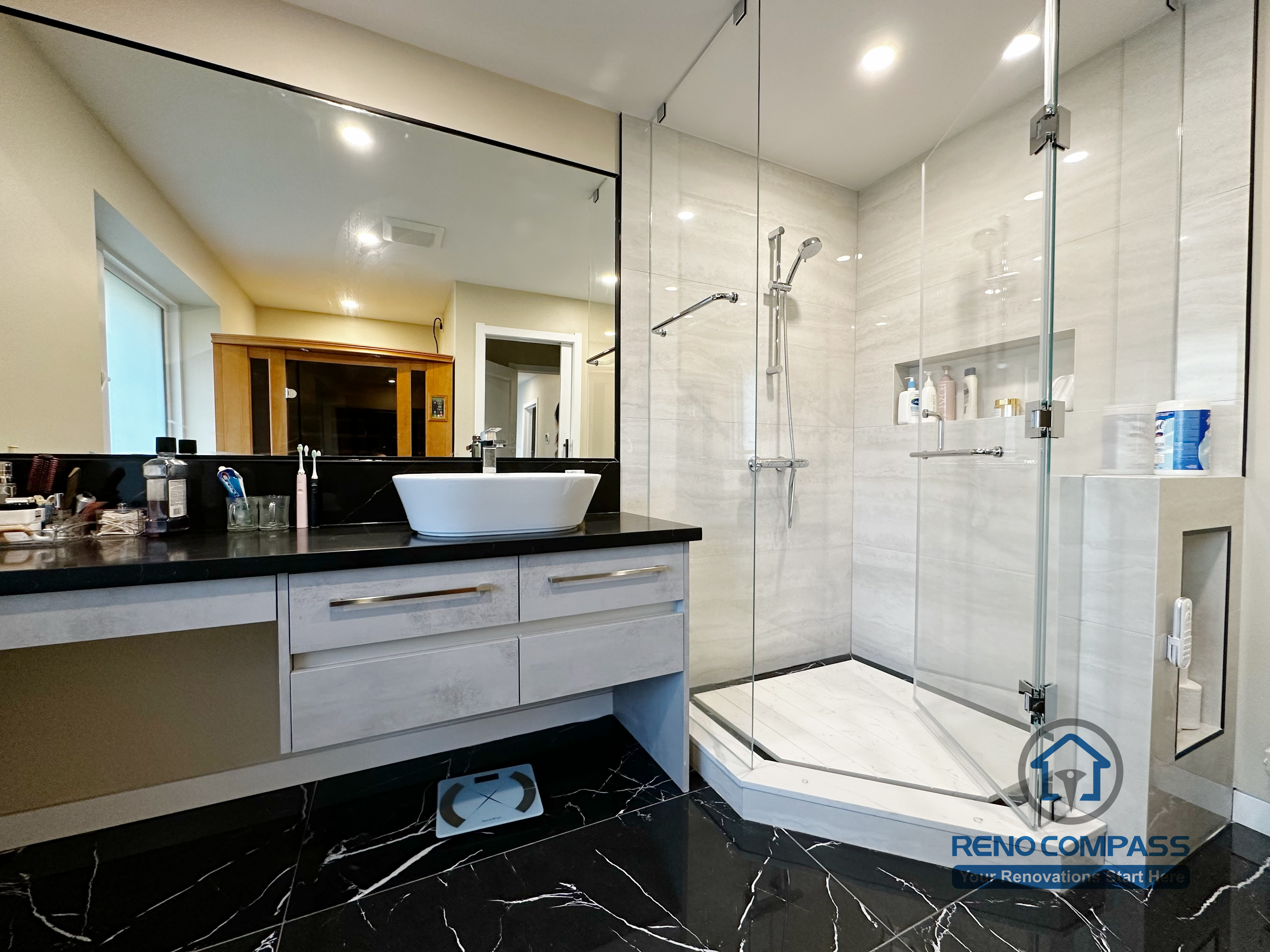 Bathroom vanity completed as part of a North York interior renovation. This design features a custom floating vanity, vessel sink, black countertop, and large wall mirror, paired with marble-look flooring and a glass shower enclosure. Built with a focus on durability, clean detailing, and daily usability by a professional Toronto renovation company.