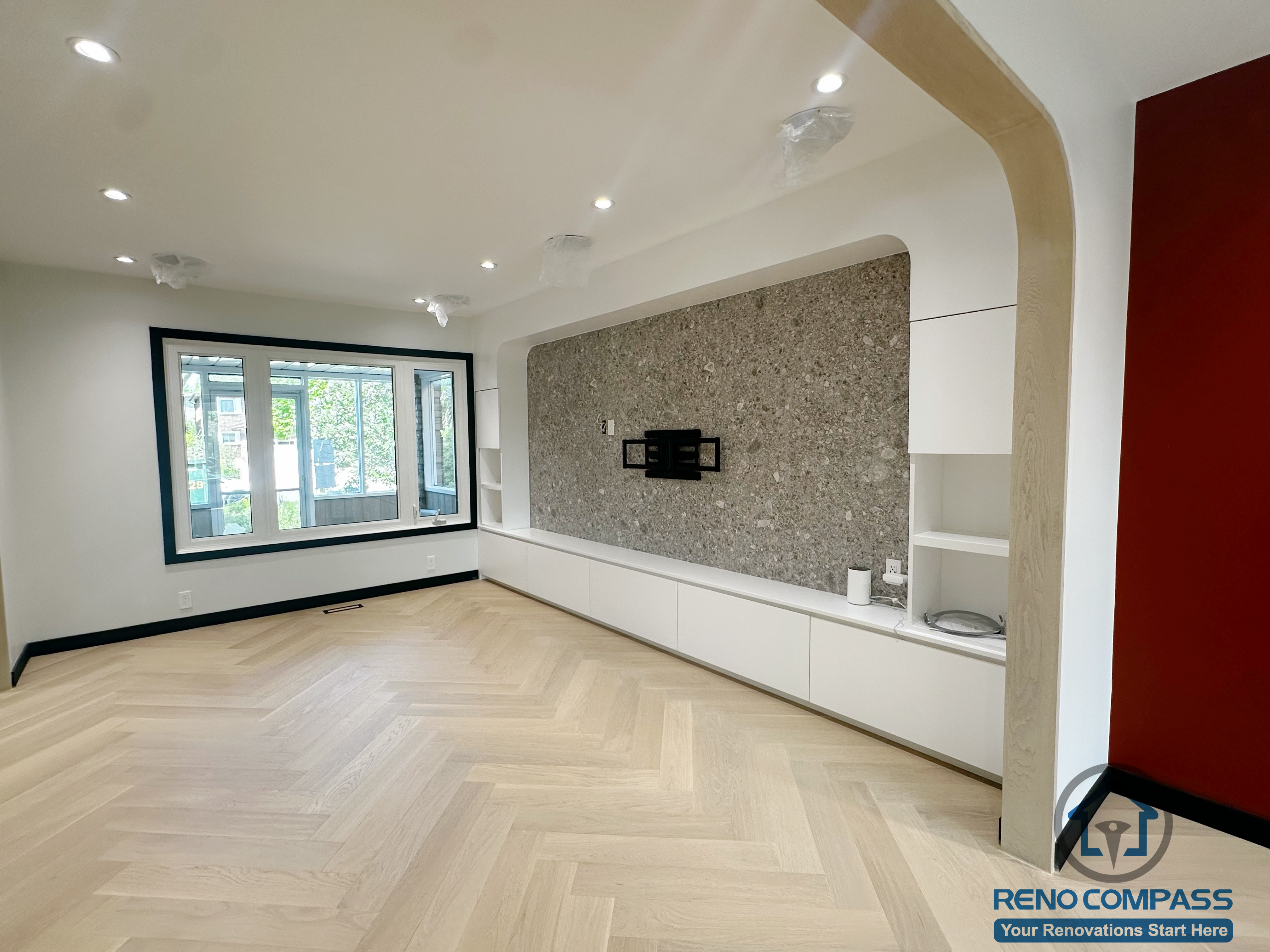 This photo shows another angle of the Richmond Hill living room renovation, featuring both the large window and the modern feature wall.
The light herringbone flooring elevates the overall texture of the space, while the stone TV wall and extended white cabinetry create a clean and contemporary aesthetic.
The soft curved doorway adds architectural character and enhances the room’s visual layers.