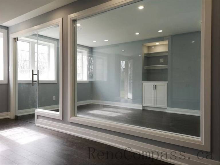 This contemporary basement renovation in Aurora features floor-to-ceiling mirrors, a sleek glass partition, recessed lighting, and built-in storage cabinetry. The design enhances natural light and creates an open, spacious atmosphere — expertly completed by Reno Compass.