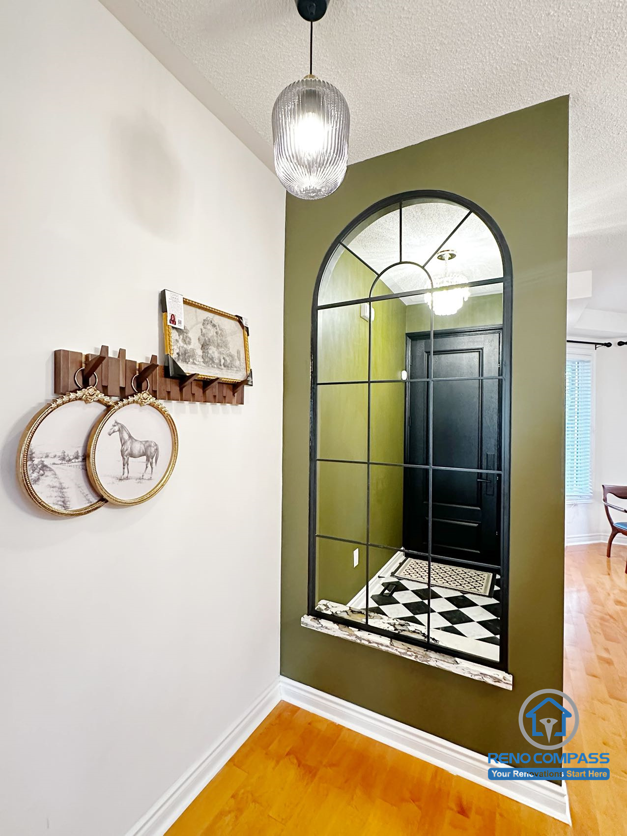 This interior renovation highlights a refined entryway accent wall finished in deep green, paired with a large arched mirror framed in black metal. The mirror reflects the checkered tile flooring and entry door, enhancing light and depth within the space. Subtle wall décor and pendant lighting complete a balanced design that adds character without overwhelming the layout.