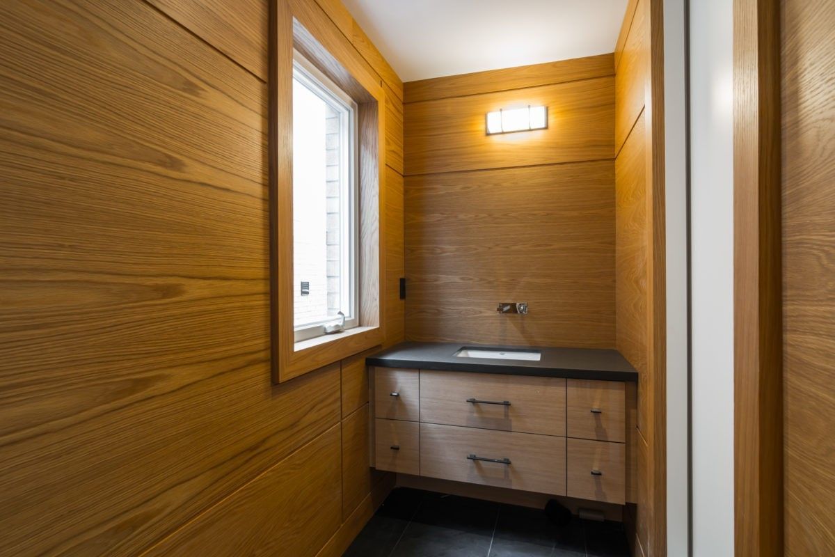As part of this 4,500 sq ft modern interior renovation in Toronto, this custom powder room highlights refined craftsmanship and architectural warmth. The space features full-height wood paneling, a floating vanity with sleek hardware, and a minimalist countertop design that enhances visual clarity. Natural light from the window balances the rich wood tones, creating a serene and contemporary atmosphere. Completed by a professional Toronto Renovation Company, Reno Compass Inc., this project demonstrates precision detailing and high-end millwork integration.