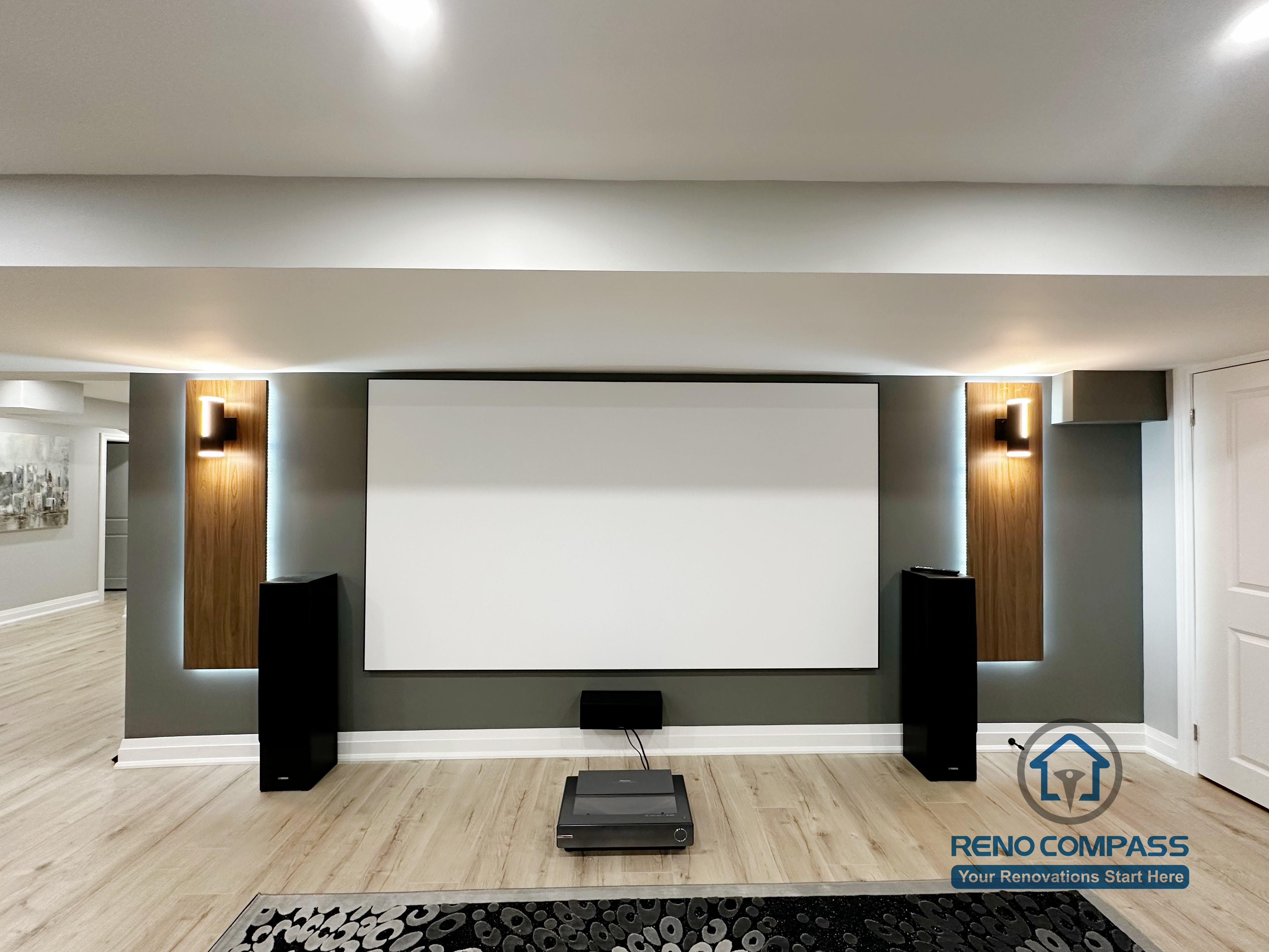 This Newmarket basement renovation features a custom home theater with a built-in projector screen, accent wall lighting, and integrated speaker placement. The finished basement is designed as a multifunctional family entertainment space, combining a modern media wall, comfortable seating area, and durable flooring for everyday use and movie nights.