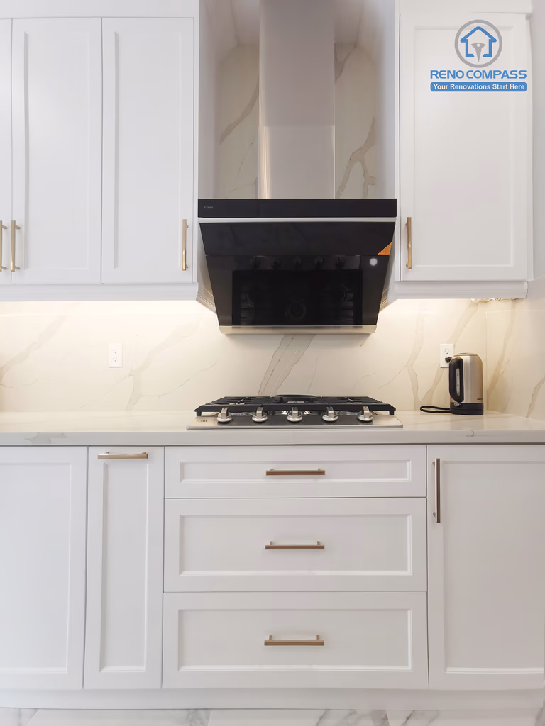 This Markham interior renovation highlights a well-organized kitchen cooking zone designed for efficiency, safety, and visual balance. The layout features a built-in gas cooktop paired with a sleek, modern range hood that provides effective ventilation while maintaining a clean elevation. White shaker cabinetry with warm metal hardware frames the space symmetrically, offering ample storage and a refined, timeless appearance. The full-height stone-look backsplash enhances durability and visual continuity across the work surface. Completed by Reno Compass, this kitchen renovation demonstrates a thoughtful approach to functional zoning, proportion control, and long-term usability for modern Markham homes.