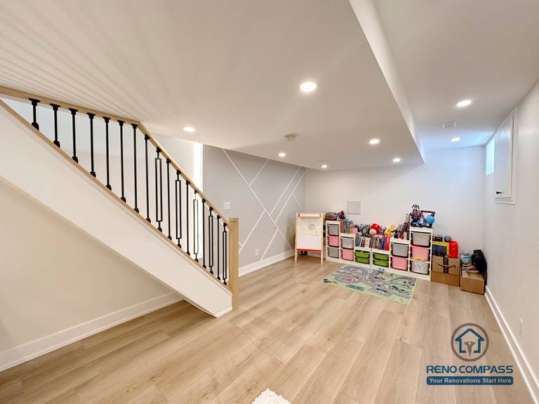 This image showcases a completed Toronto basement underpinning and renovation project, featuring an open-concept layout with upgraded staircase, modern railing, recessed lighting, and durable engineered flooring. The basement excavation increased ceiling height, creating a brighter and more functional living space suitable for family use, play areas, or future multi-purpose rooms. Ideal for homeowners looking for professional basement lowering and renovation solutions in Toronto.