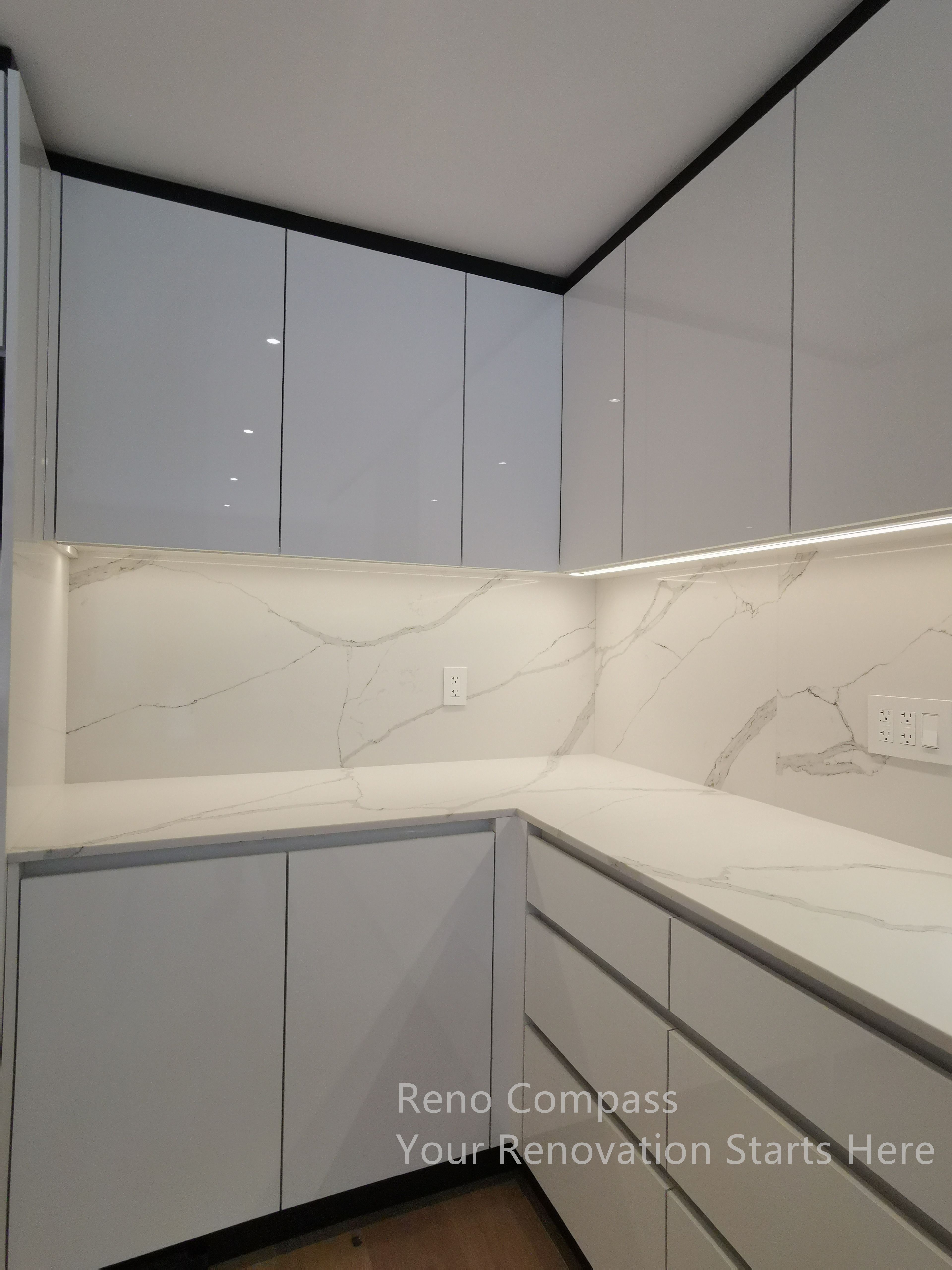 This image highlights the custom kitchen cabinetry completed as part of a Markham interior renovation. The sleek, handle-less upper cabinets create a clean and modern visual line, while integrated under-cabinet lighting enhances both functionality and ambiance. A marble-look stone backsplash and matching countertop provide durability and visual continuity, resulting in a refined, low-maintenance kitchen design tailored for everyday use.