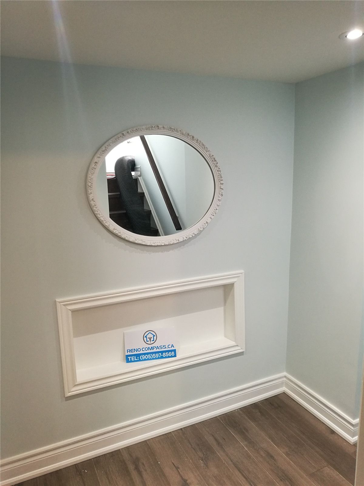 Basement interior renovation detail in Pickering featuring a custom recessed wall niche, decorative round mirror, fresh paint, and wood-look flooring. This subtle design upgrade adds character and functionality to the living space, completed by a professional Toronto renovation company.