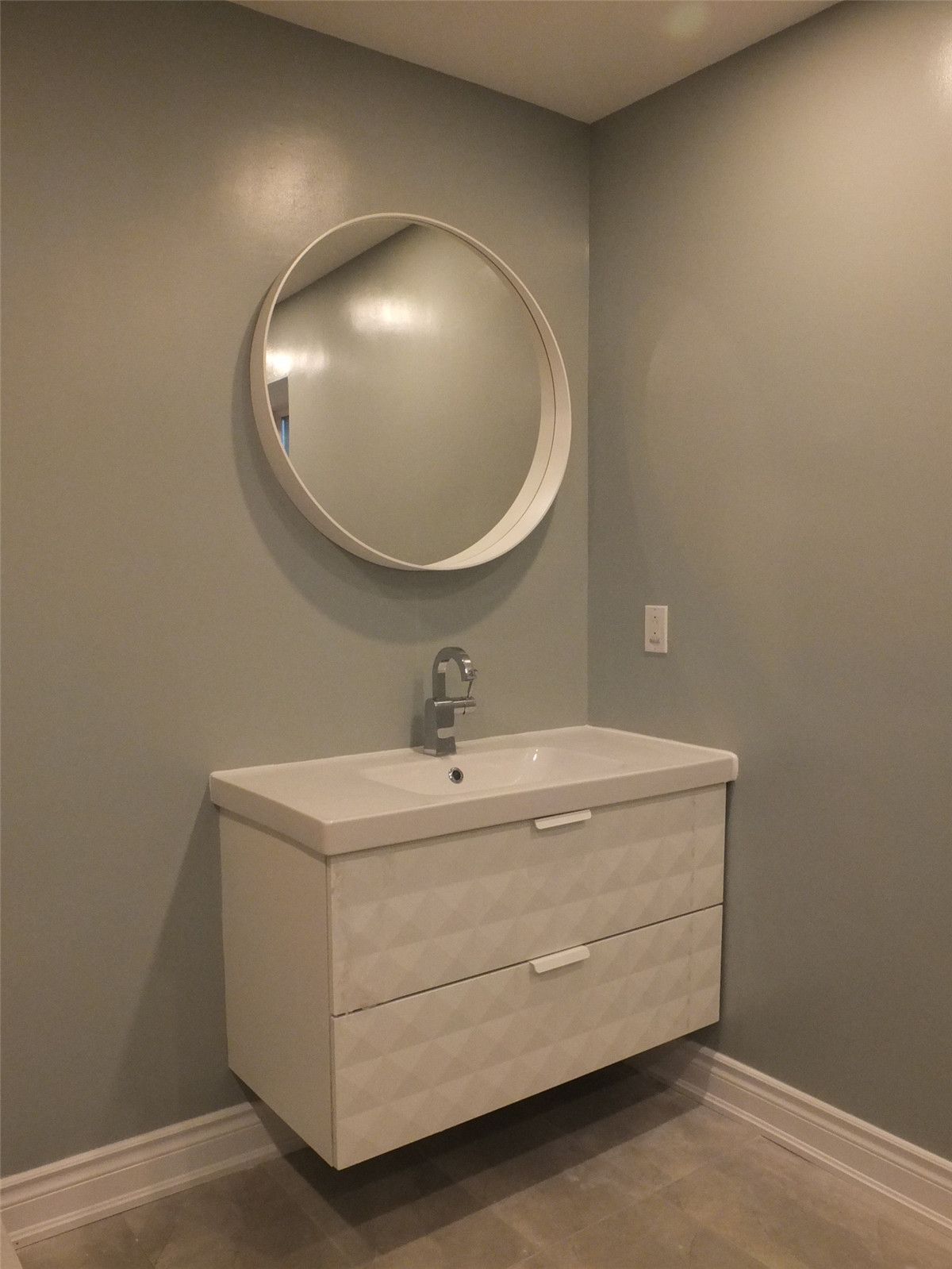 This image highlights a modern bathroom vanity renovation as part of a Mississauga interior renovation project. The design features a floating vanity with integrated drawers, a sleek single-handle faucet, and a round wall-mounted mirror that enhances visual balance. Soft neutral wall tones and minimalist finishes create a clean, contemporary look while maintaining functionality. Completed by a professional Toronto renovation company, this bathroom upgrade improves storage efficiency, space optimization, and overall interior aesthetics for Mississauga homes.