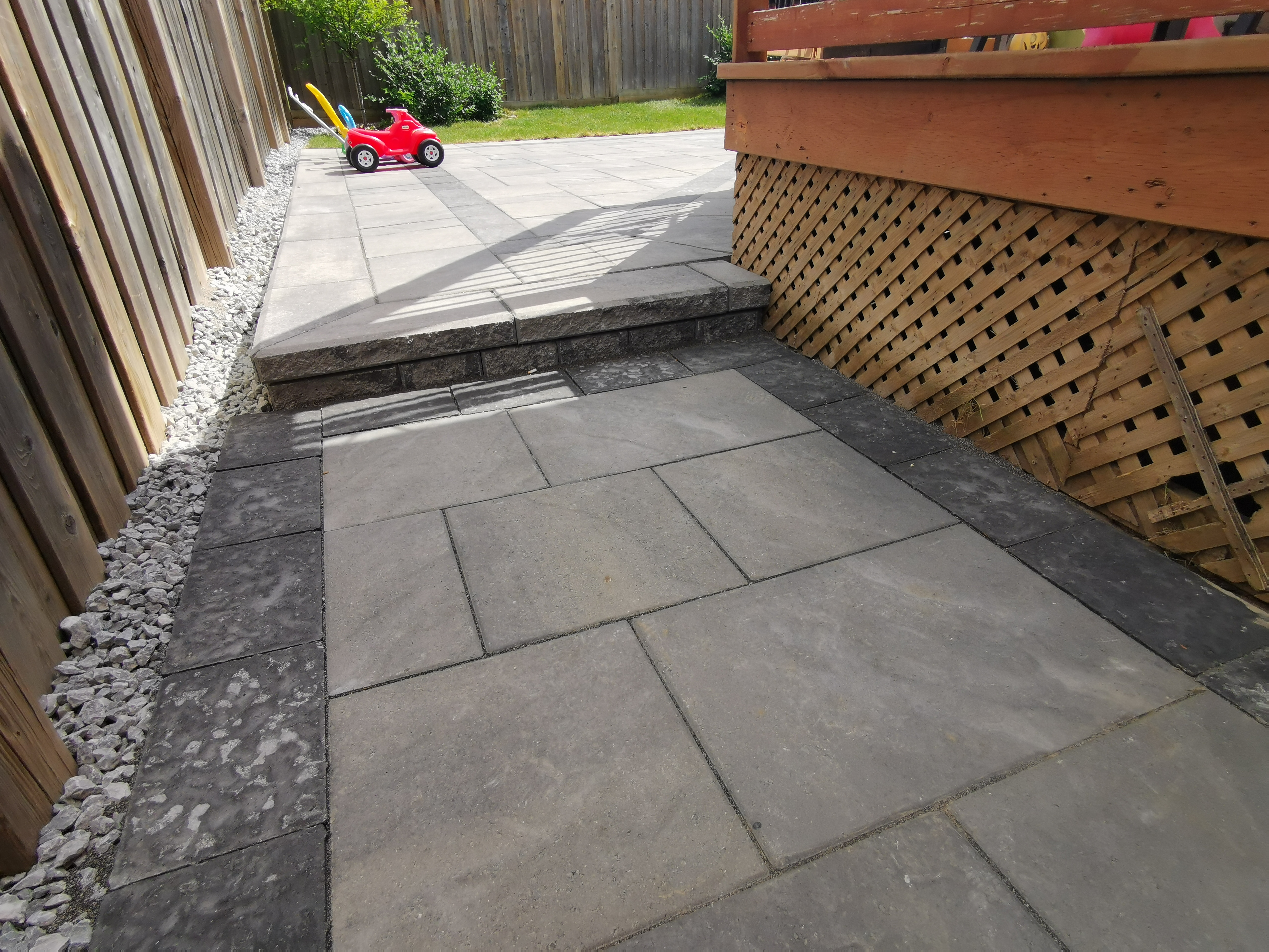 This Aurora backyard interlocking project features a spacious paver patio seamlessly connected to a raised wooden deck. Large-format concrete pavers provide a durable, level surface ideal for outdoor activities, family gatherings, and everyday use. The clean layout enhances drainage and long-term performance while maintaining a modern and low-maintenance finish. The interlocking patio creates a functional and inviting outdoor living space, perfectly suited for residential backyards in Aurora.