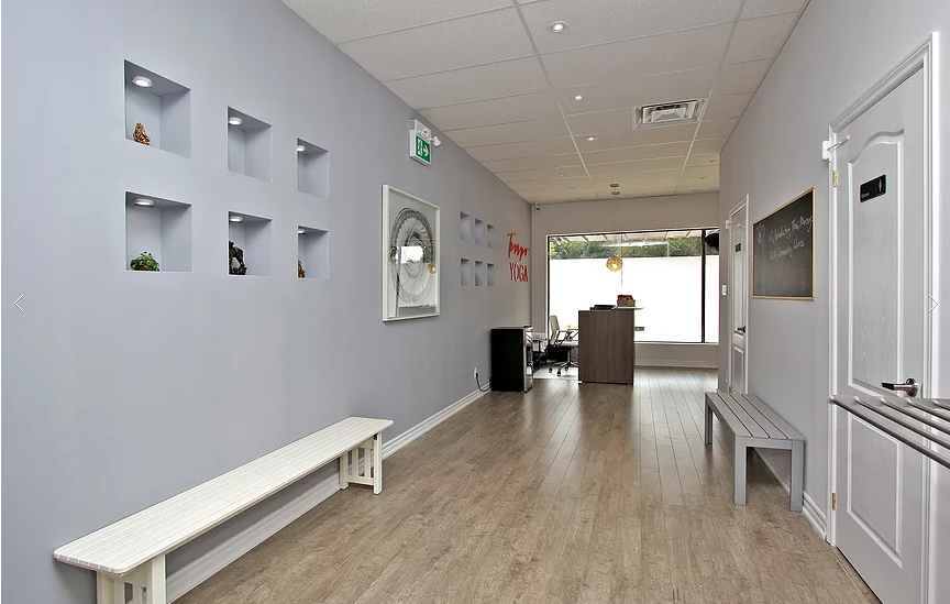 Spacious interior hallway and reception view of a newly renovated Richmond Hill yoga studio commercial space. This renovation features wood-look flooring, custom recessed display niches with accent lighting, modern ceiling upgrades, and clean neutral wall finishes to create a calming and functional wellness environment. Designed to improve client flow and visual appeal, this project was completed by a professional Toronto renovation company specializing in boutique commercial and fitness studio renovations.