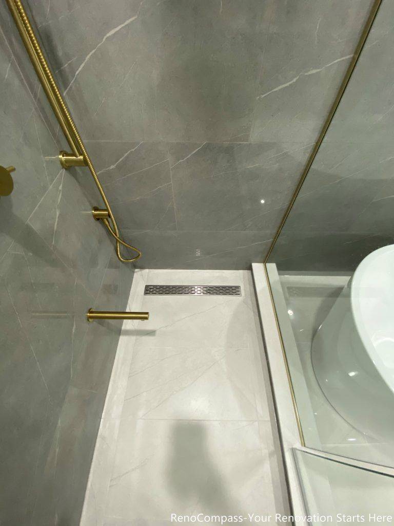 This Oakville master bathroom renovation highlights a modern walk-in shower with sleek linear floor drain, large-format porcelain tiles, and premium gold shower fixtures. The clean tile layout, precise slope for drainage, and frameless glass enclosure create a seamless and contemporary spa-style shower experience. Completed by a trusted Toronto renovation company, this bathroom upgrade focuses on waterproofing quality, functionality, and elegant design, delivering a durable and visually refined space that enhances everyday comfort and home value.